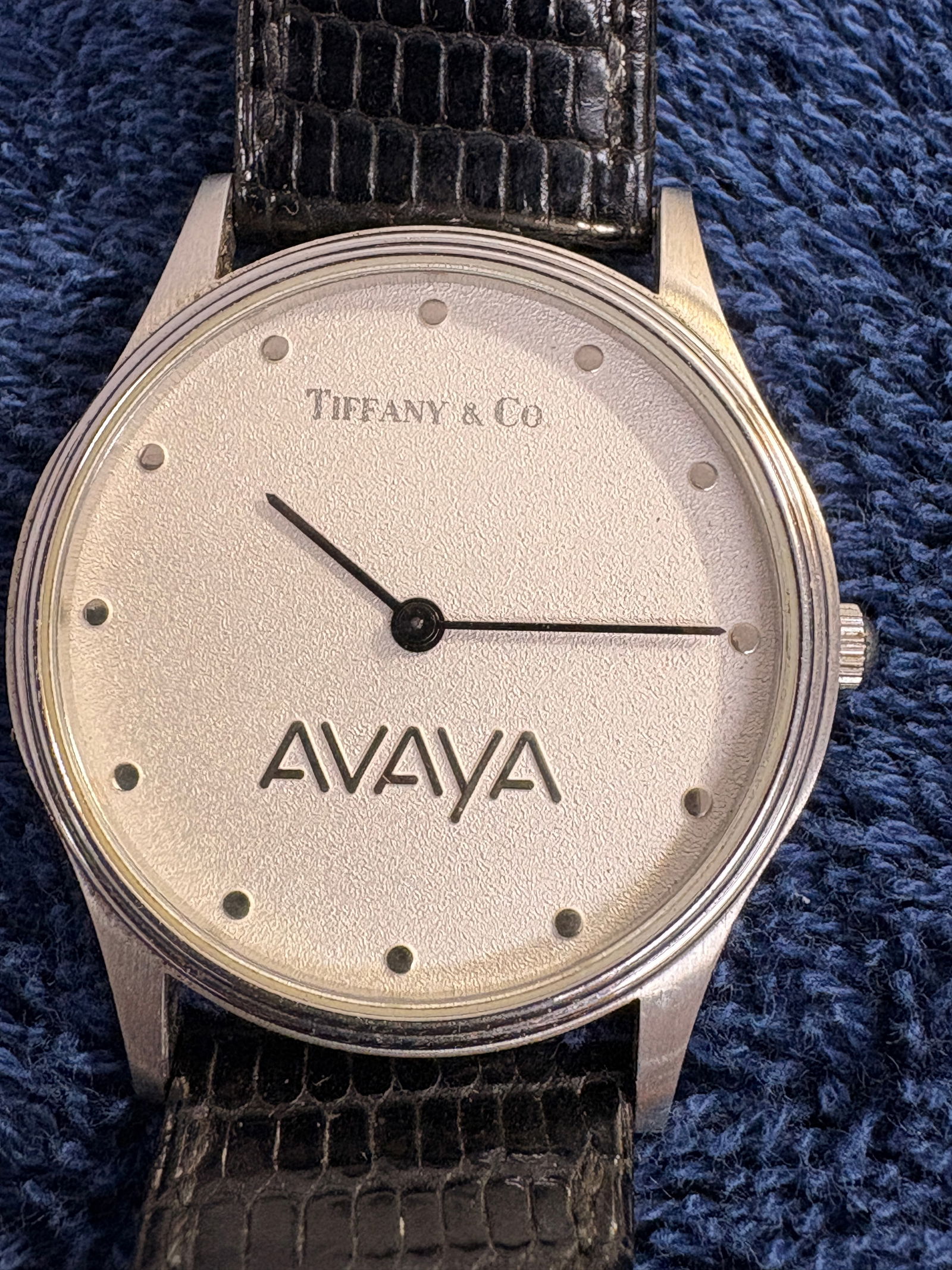 Portfolio by Tiffany & Co. Swiss Quartz Dress Watch (Avaya Dial): Portfolio by Tiffany & Co. Swiss made quartz dress watch featuring a minimalist champagne dial with dot hour markers and co-branded AVAYA logo. Slim stainless steel case fitted with black leather