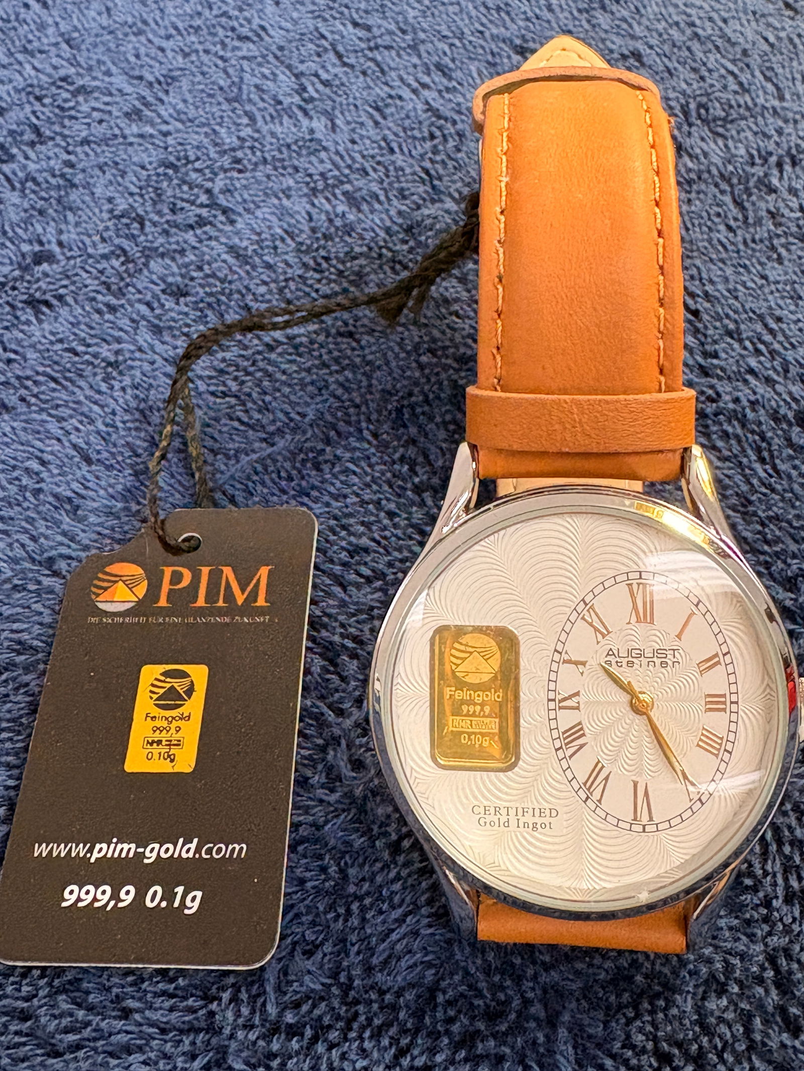 August Steiner Gold Ingot Dial Quartz Wristwatch: August Steiner quartz wristwatch featuring a genuine .999 fine gold ingot (0.1 g) set into the patterned dial. Roman numeral sub-dial, polished case, and tan leather strap. Approx. 42 mm case.