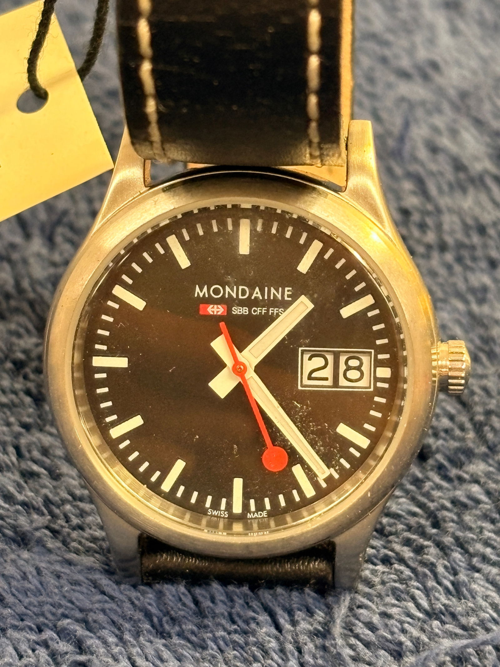 Mondaine SBB CFF FFS Swiss Railway Date Wristwatch: Iconic Mondaine Swiss Railway watch with black dial, bold white markers, and signature red seconds hand. Stainless steel case with date window and black leather strap. Swiss made quartz movement.