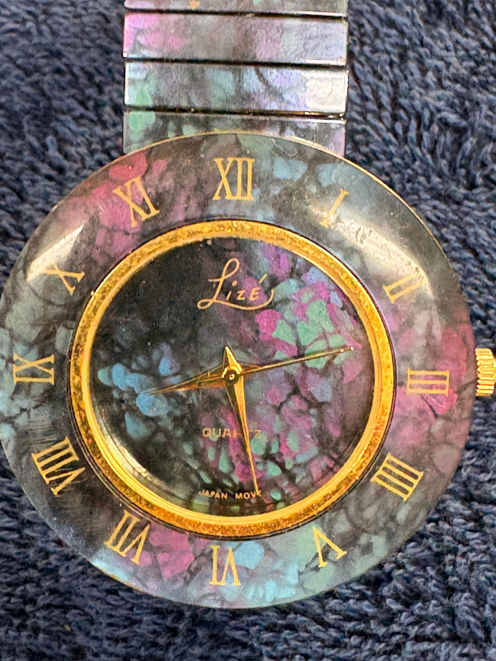Lize Quartz Wristwatch (Japan Movt): Lize quartz wristwatch featuring a multicolor stone-style dial and bezel with Roman numerals, gold-tone hands and case, and stretch metal bracelet. Dial marked “Quartz – Japan Movt.” Approx.