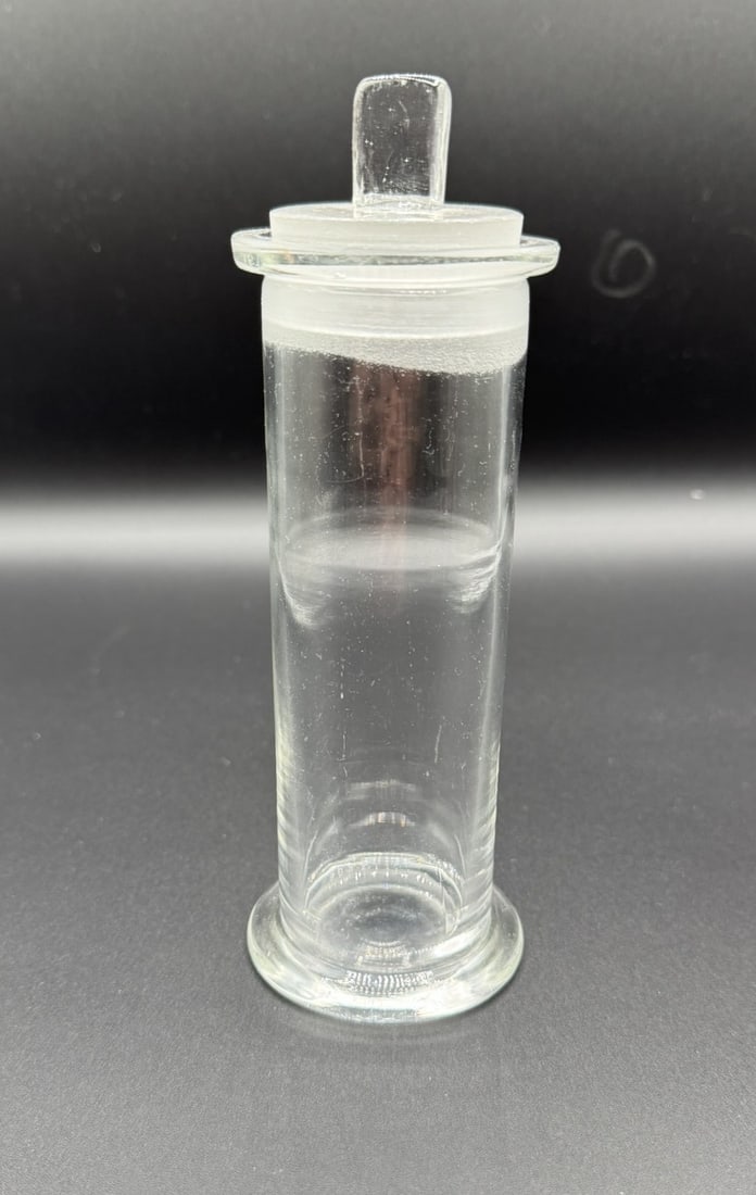 Vintage Clear Glass Apothecary Bottles with Ground Glass Stoppers: Offered here is a vintage clear glass apothecary or laboratory bottle featuring a cylindrical form and original flat ground glass stopper. This piece likely dates to the early to mid-20th century and