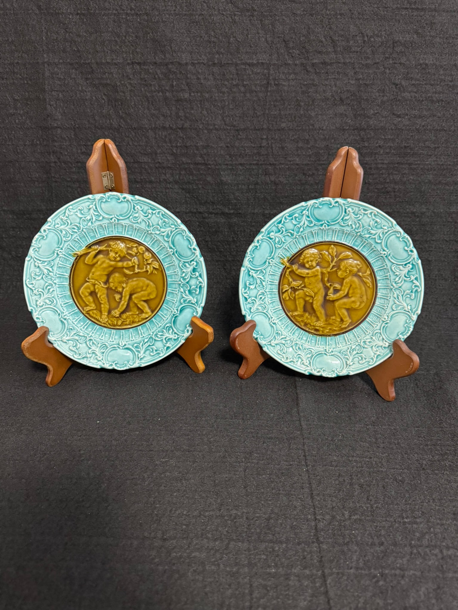 Antique Villeroy & Boch Mettlach Majolica Wall Plaques: This is a matched pair of antique majolica wall plaques made by Villeroy & Boch at their renowned Mettlach factory. Each 7.5-inch plate features a central brown medallion with playful putti figures in