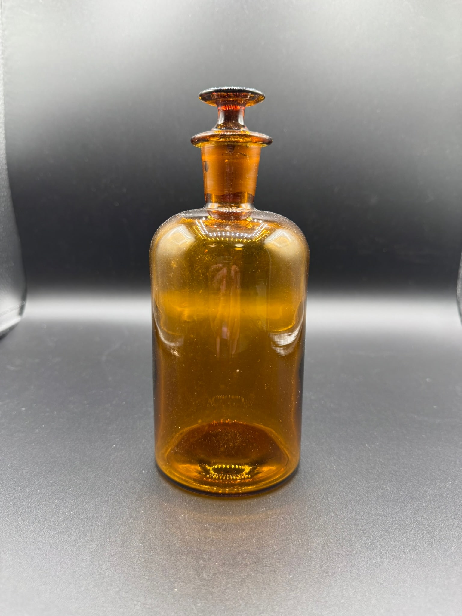 Antique Amber Apothecary Bottle with Ground Stopper: Offered here is a striking amber glass apothecary bottle measuring approximately 7.5 inches tall, complete with its original ground glass stopper. This cylindrical bottle features: Rich amber colorati