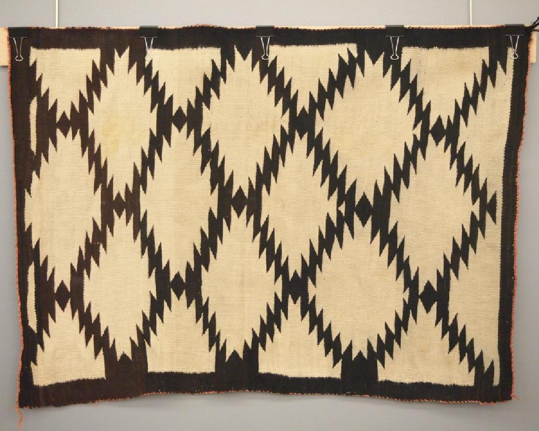 Navajo weaving/rug: A 4.6 x 3.4' early 20th century Navajo weaving/rug. Handspun wool, a serrated diamond pattern overall in brown and natural white. The edges are bound in red (faded). Minor wear; several stains; two co