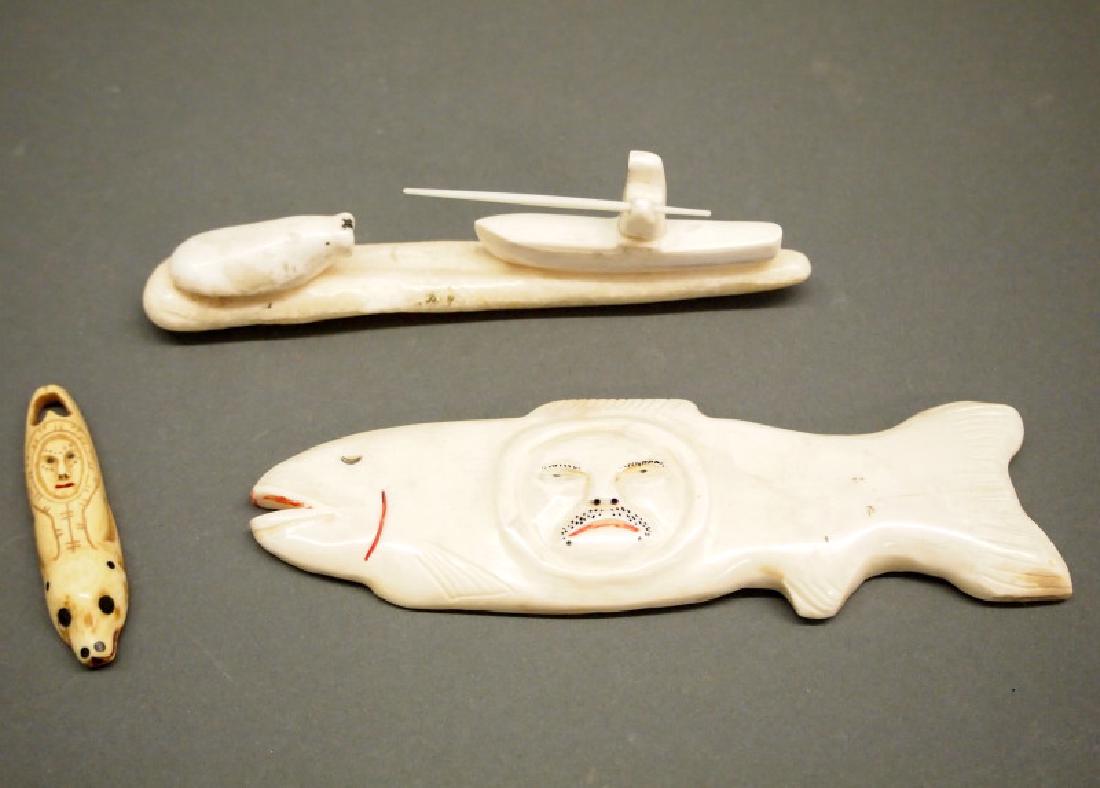 3 Inuit walrus carvings: Three Inuit walrus tusk carvings. Including 1 fish with a male face at the center, red and black painted accents; 1 figure in a kayak preparing to spear a walrus; and 1 amulet with a human face and be