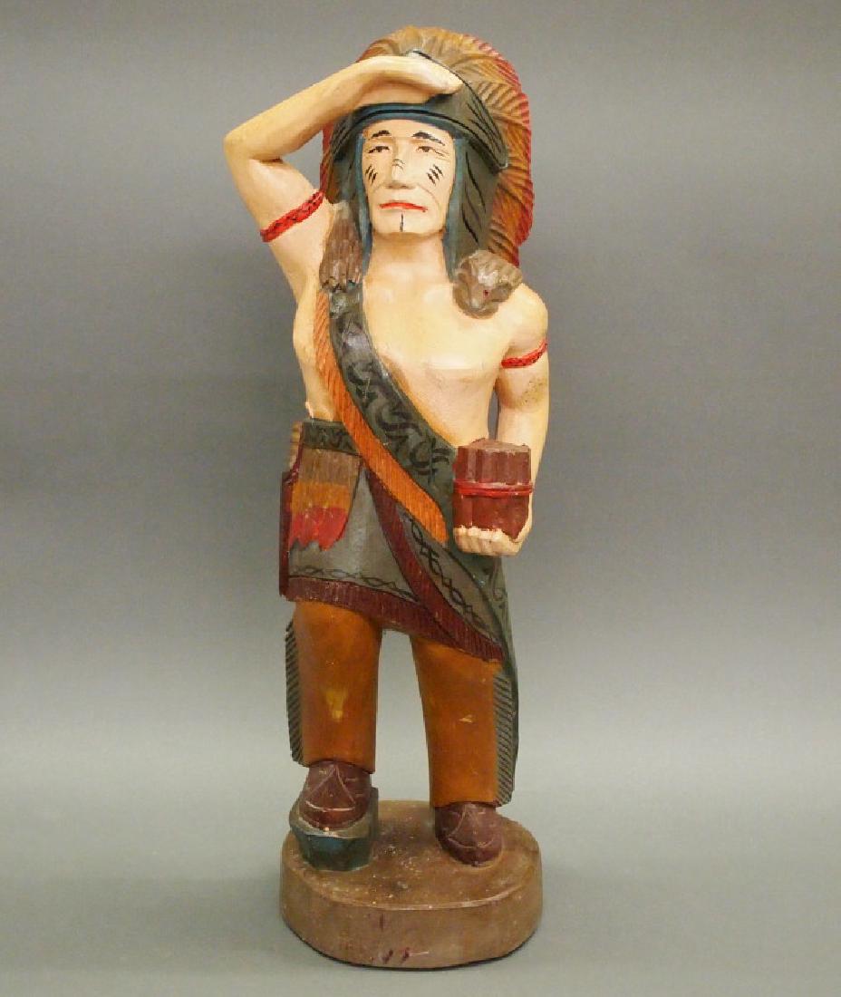 Cigar store Indian: A carved and painted wood tobacconist figure of an Indian. Cigar store-type, modeled with his right hand shading his eyes, and holding a bundle of cigars in his left. No apparent markings. Small area