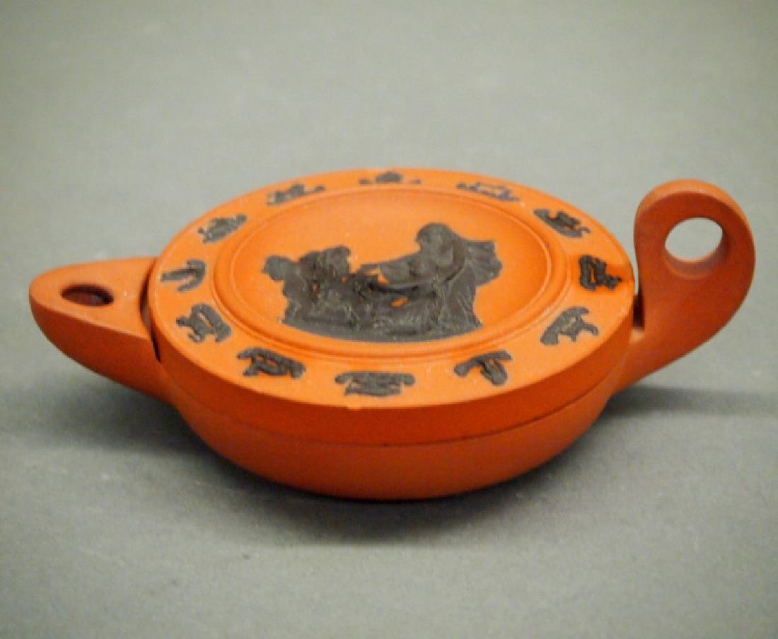 Wedgwood Rosso Antico oil lamp: An early 19th century Wedgwood Rosso Antico oil lamp and cover. Decorated in black cameo relief with a classical scene at the center, bordered by the symbols of the zodiac. Impressed "Wedgwood" undern