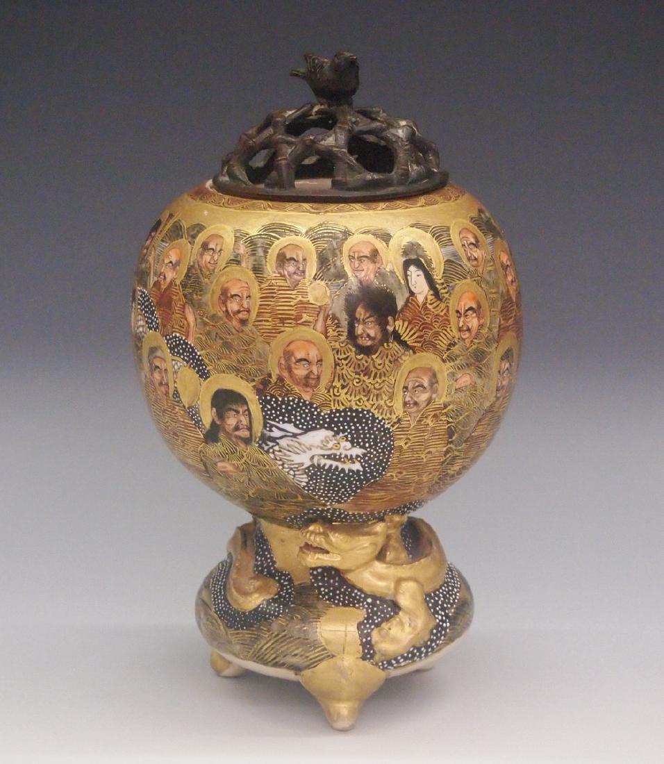 Japanese Satsuma Censer: A Japanese Satsuma Censer. Having a pierced patinated metal cover with bird form finial atop a bulbous body which rests on a circular base that is raised on three feet. Decorated overall with the "Tho