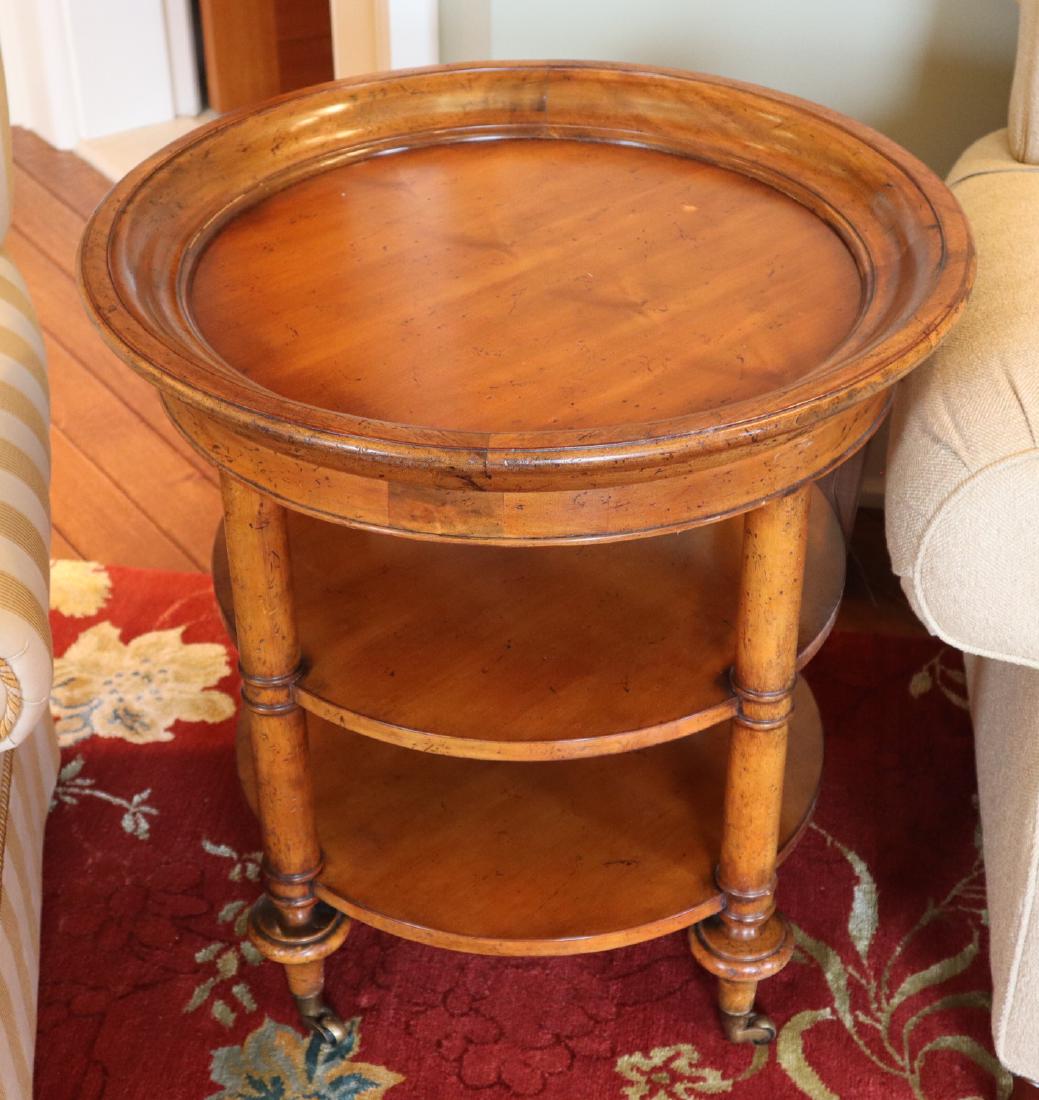 Baker End Table: A Baker Milling Road Collection End Table. Round table with two shelves; supports are on casters. Light wear to finish. 26" x 27" h. ESTIMATE $100-200