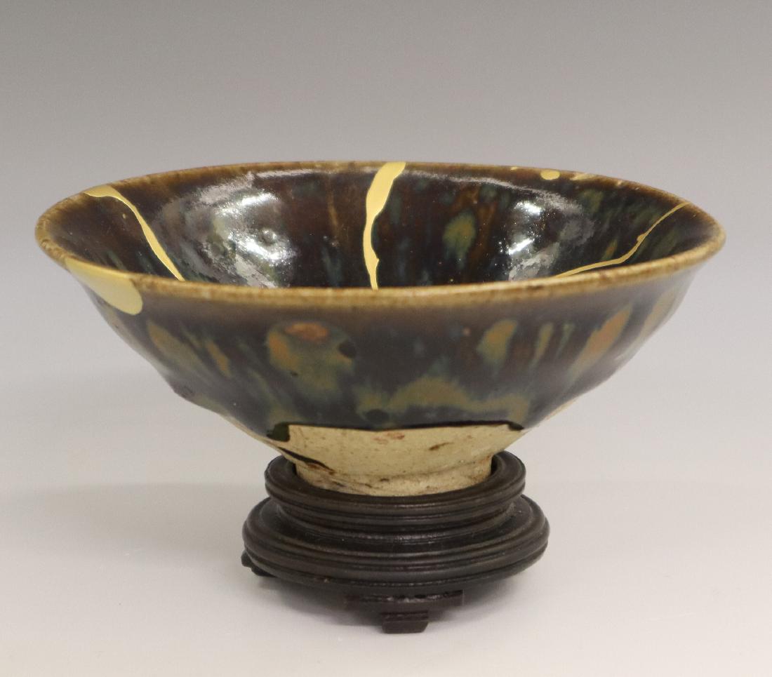 Chinese Earthenware Tea Bowl: A Chinese Earthenware Tea Bowl. Having a brown ground with smatterings of orange and blue/green glaze. Unmarked, includes a wood stand. Repaired condition. 4 5/8" diameter x 1 3/4" high. ESTIMATE $400
