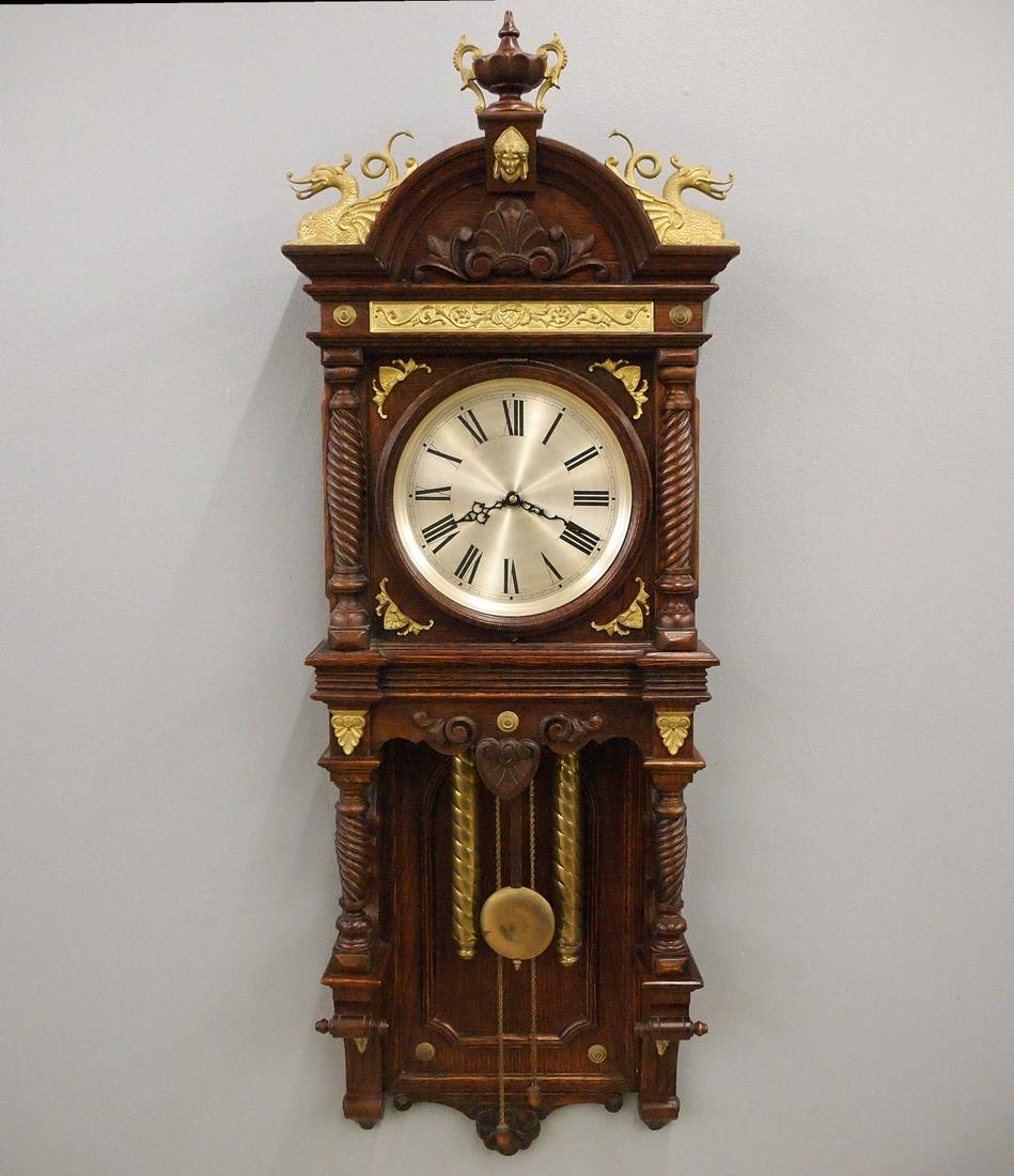 Waterbury Augusta Wall Clock: A late 19th century Waterbury "Augusta" model wall clock. 8-day weight driven time and strike movement with metal dial. Oak case with applied Brass ornamentation, turned columns and finials. Refinishe