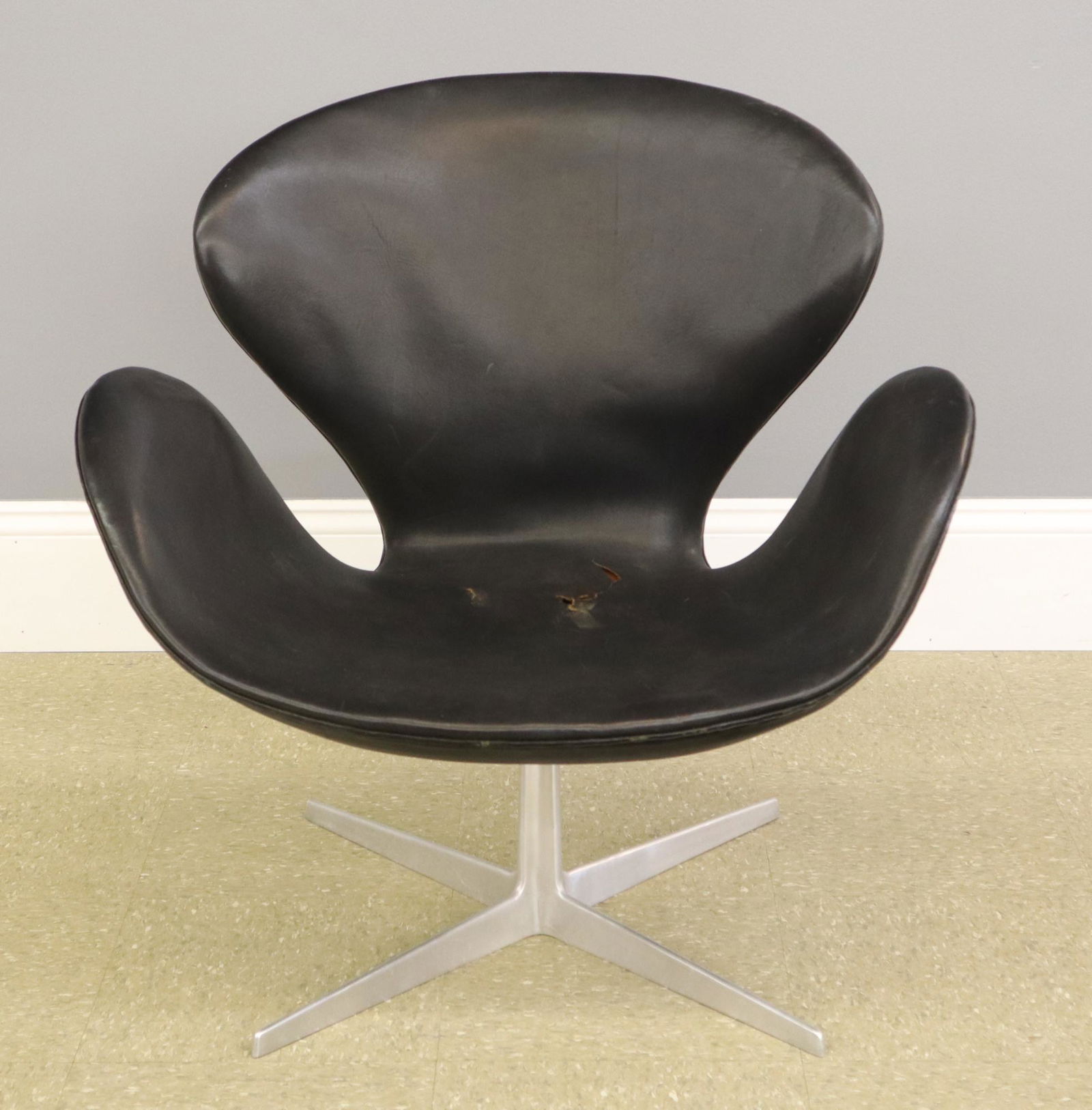 Arne Jacobsen Swan chair: A Mid Mod "Swan" chair by Arne Jacobsen for Fritz Hansen. Shaped leather covered shell on a metal base. Wear and damage to the leather including a puncture in the side and split in the seat. 29" high.