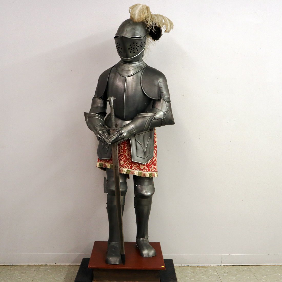 Suit Of Armor: A 1960's era suit of armor. Life size metal suit with articulated elbows and knees, hinged fittings and helmet with lift up face plate on a wood frame and painted wooden base. Includes sword. Minor we