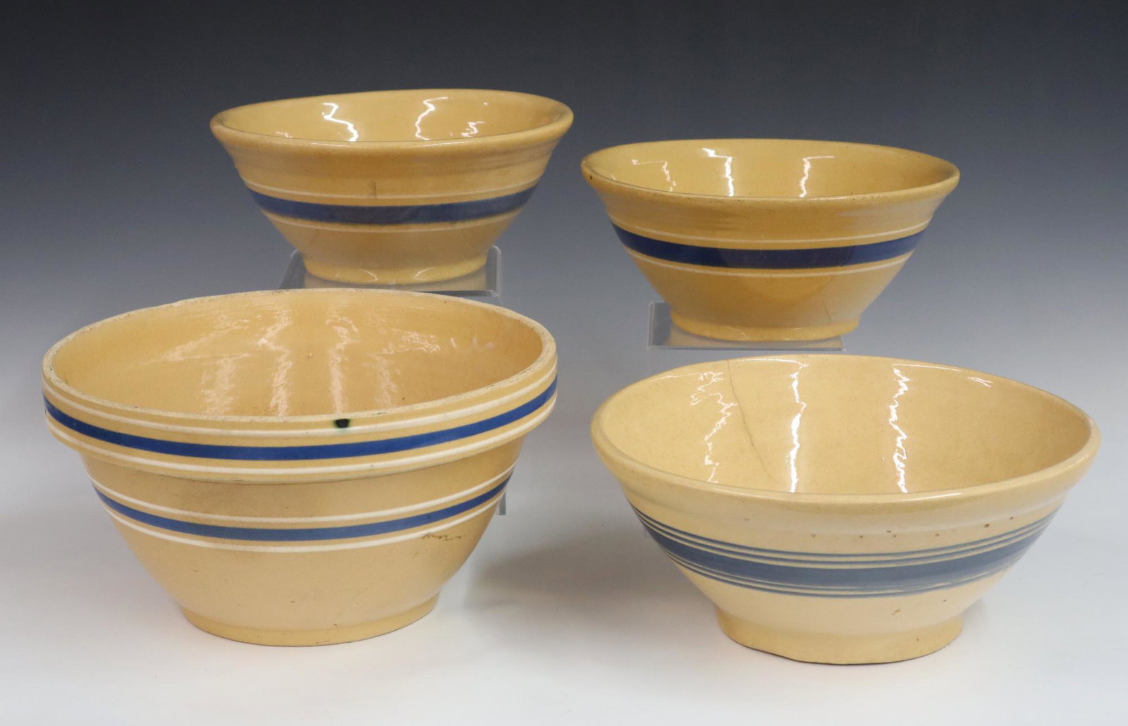 4 Yellowware Mixing Bowls: Four turn of the century Yellowware mixing bowls with similar Blue/White bands. Wear and minor edge chips, the middle two have cracks. Up to 11 1/2' diameter. ESTIMATE $50-100
