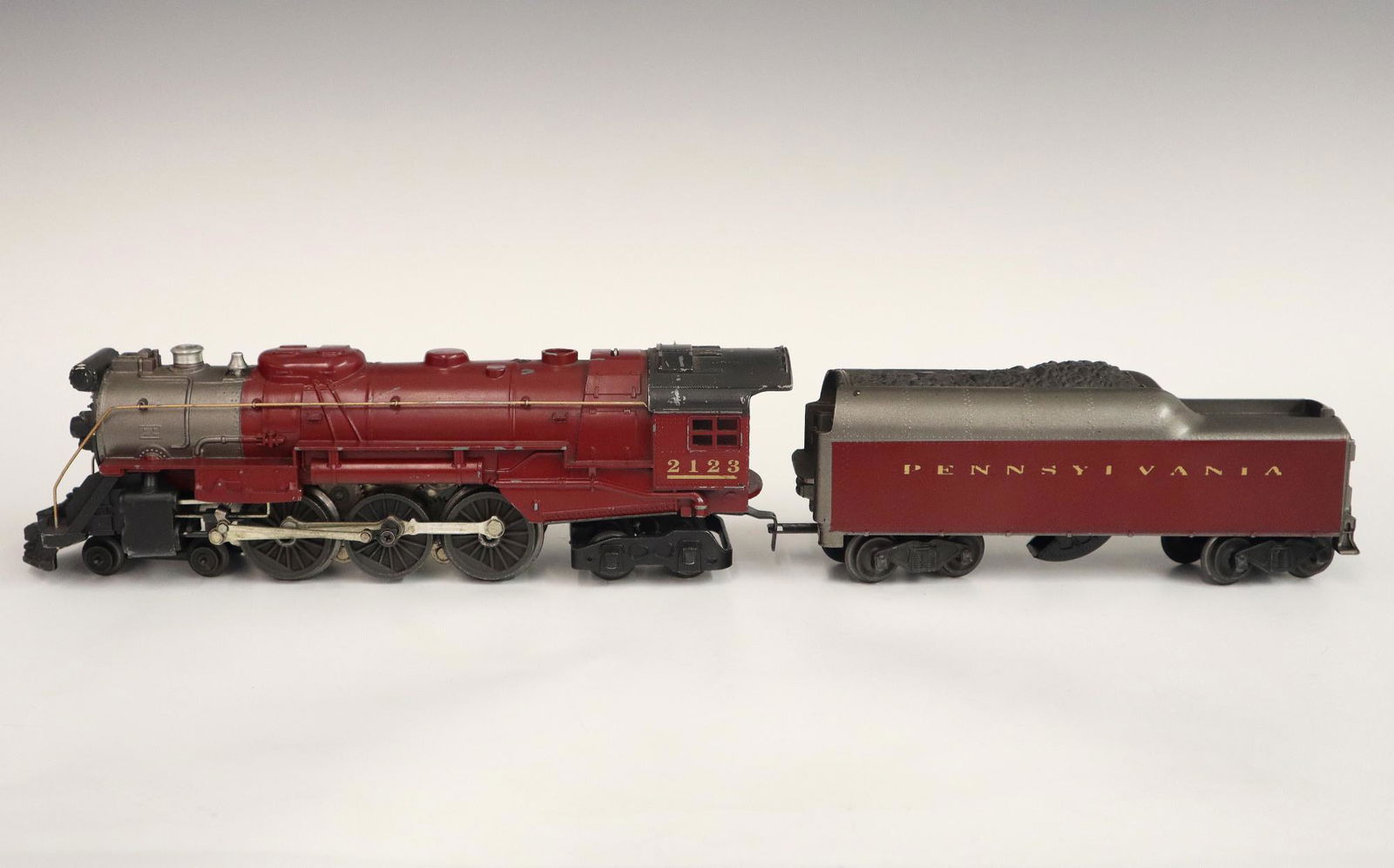 Lionel Locomotive and Tender: A Post-War Lionel O Gauge Locomotive #2123 with Tender #2046W. Maroon and silver paint. Minor wear and paint loss. 20" long overall. ESTIMATE $50-100