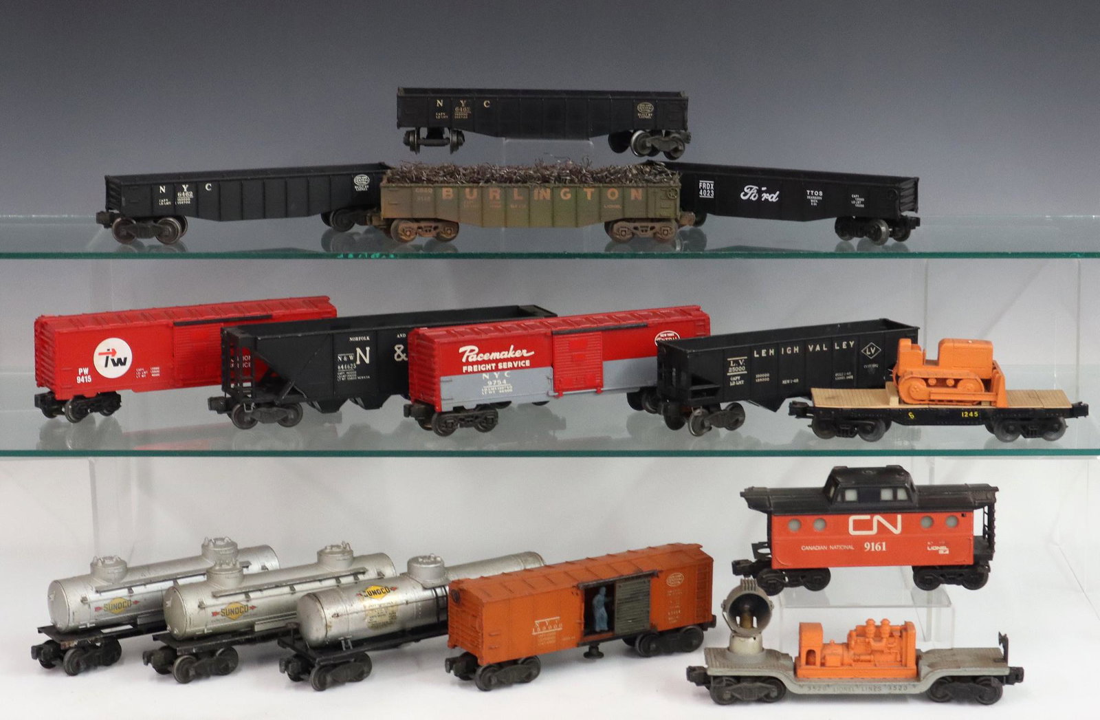 15 Lionel Train Cars: Fifteen Post- War Lionel O Gauge Train Cars. Including 3 box cars, 4 gondola cars, 2 hoppers, 3 tankers, 1 caboose, 1 search light car, and 1 flat car with bulldozer. Minor wear and soiling. Up to 11 