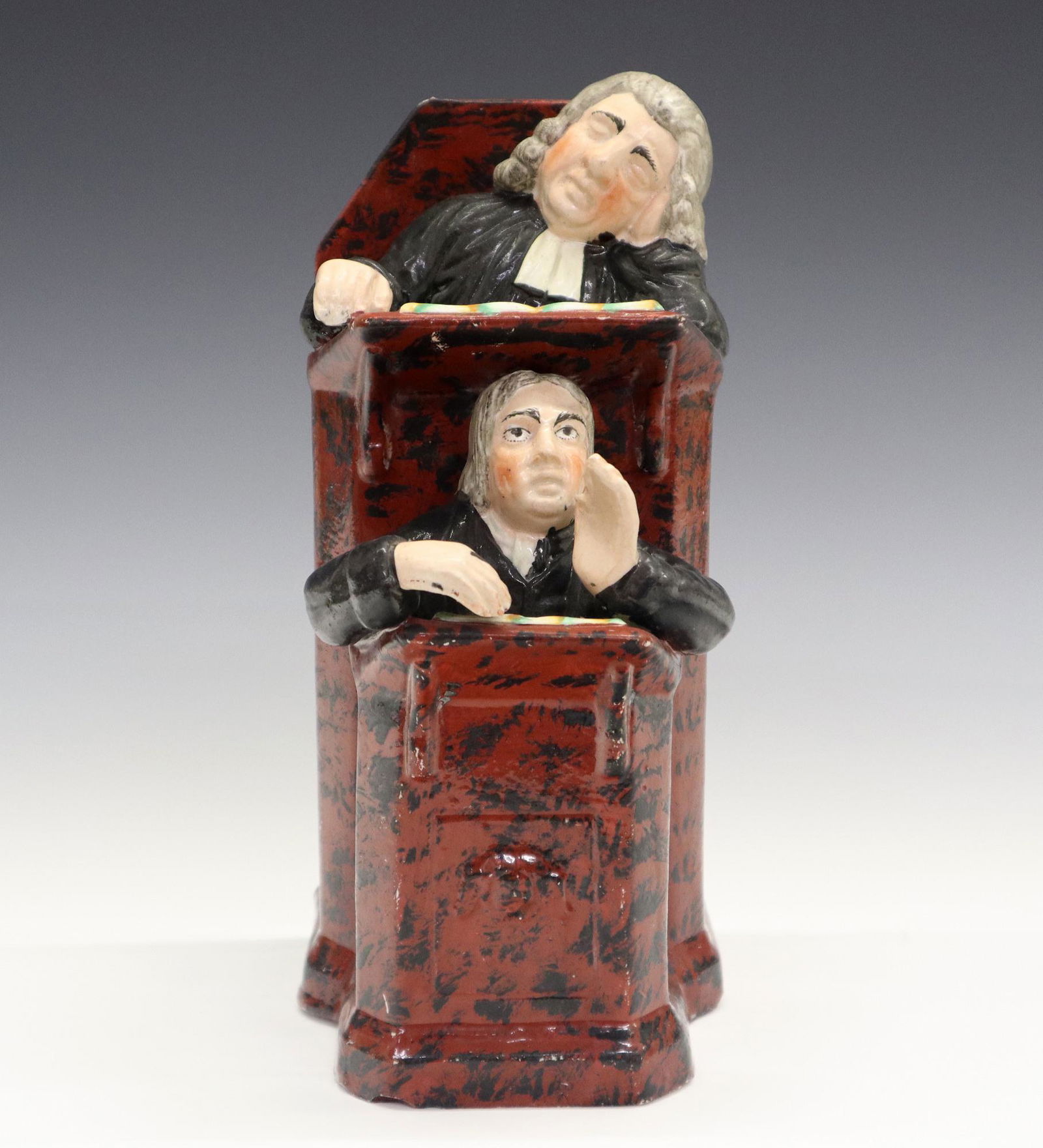 Vicar and Moses Staffordshire Figure: A 19th century Staffordshire figure entitled "The Vicar and Moses". Molded figure with two black robed figures in a brown pulpit with black brushed decoration. Minor wear, slight loss to the decoratio
