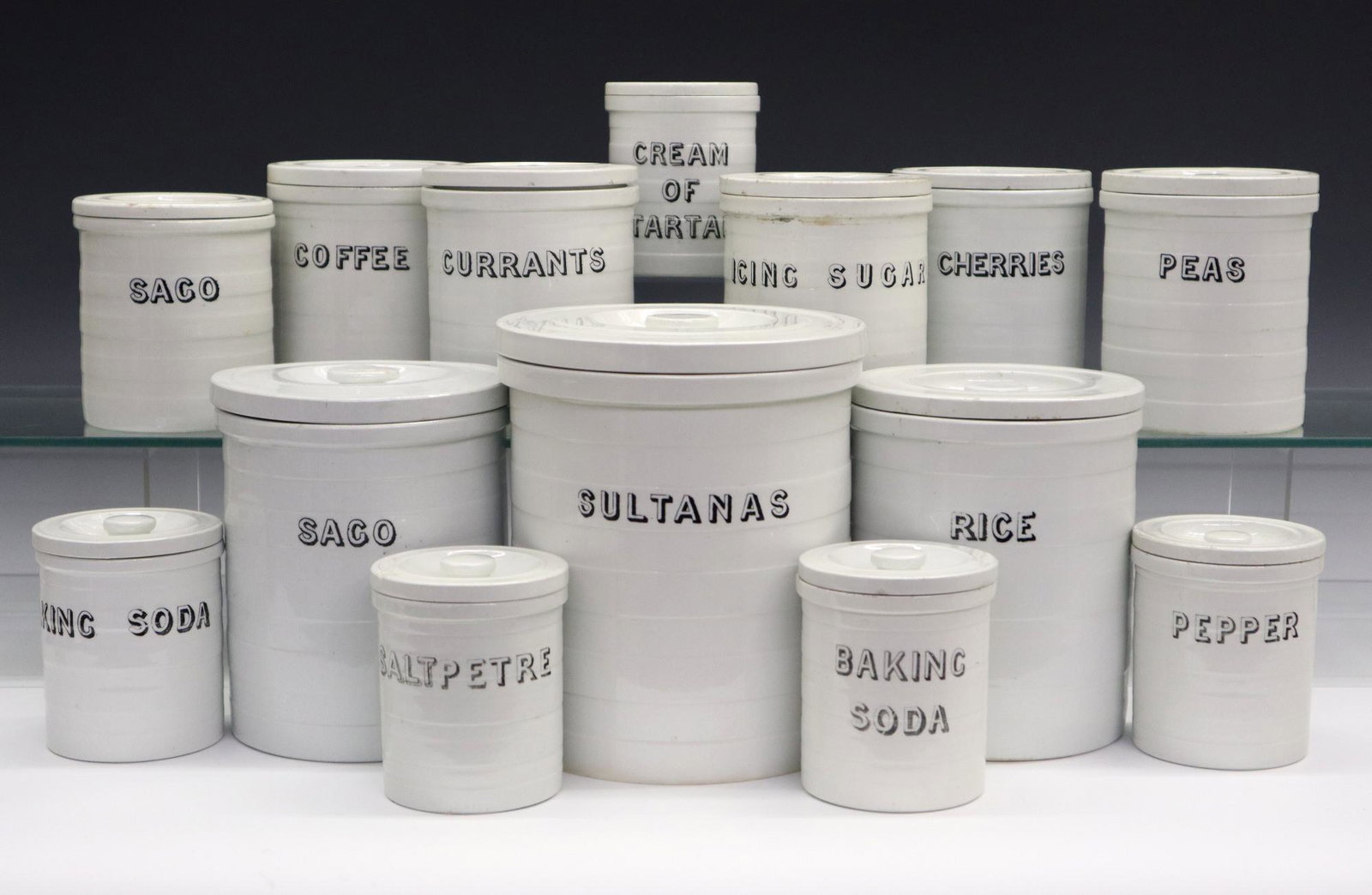 14 Maling Kitchen Canisters: A Set of Fourteen Maling Pottery/Cetem Ware Kitchen Canisters, c. 1900. White cylindrical covered canisters with black lettering including sultanas, sago, rice, icing sugar, peas, currants, cherries, 