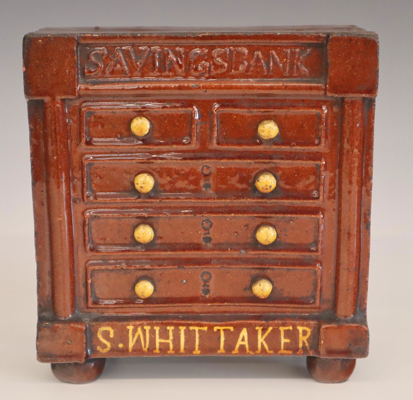 Redware Penny Bank: A 19th century Redware Penny bank with slip decoration "S. Whittaker". Molded Empire chest form with "Savings Bank" at top edge. Minor wear, small flake at one corner. 7 1/2" high. ESTIMATE $100-150