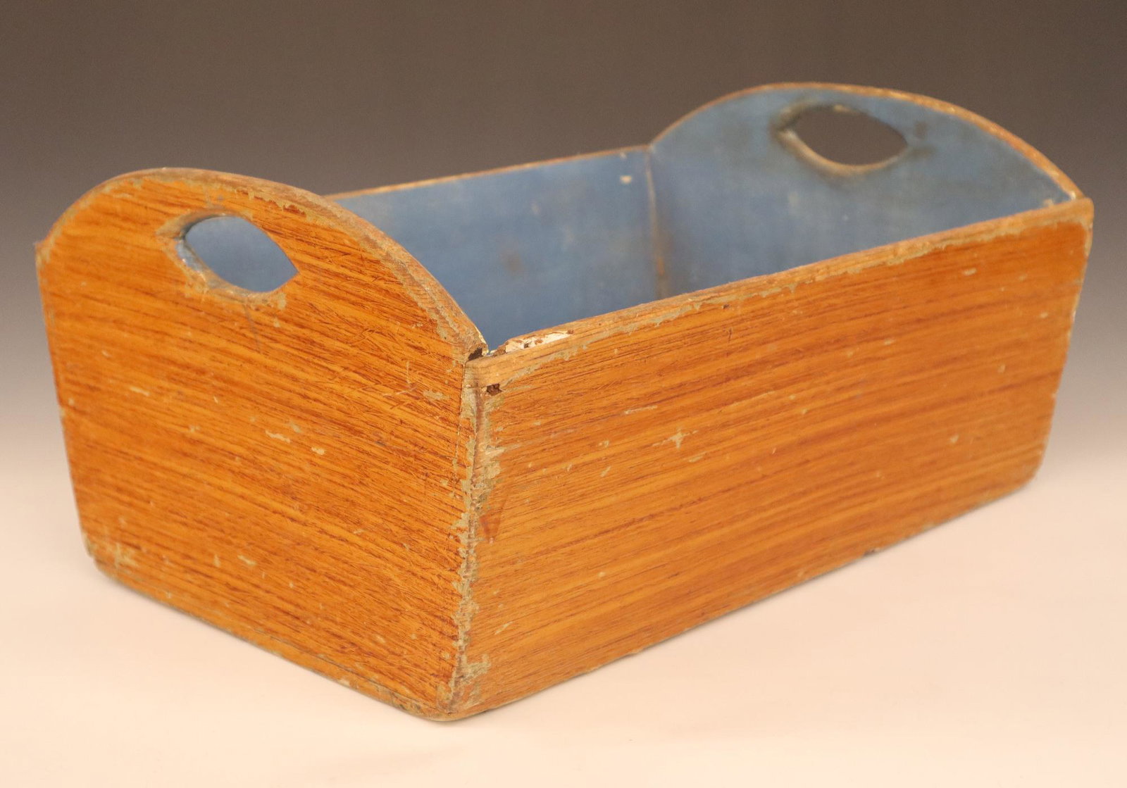 Grain Painted Wooden Tote: A turn of the century grain painted wooden tote. Shaped ends with cutout handles. Original grain painted exterior with blue interior. Wear and minor damage overall. 17 x 12 1/2 x 8 1/4" high. ESTIMATE