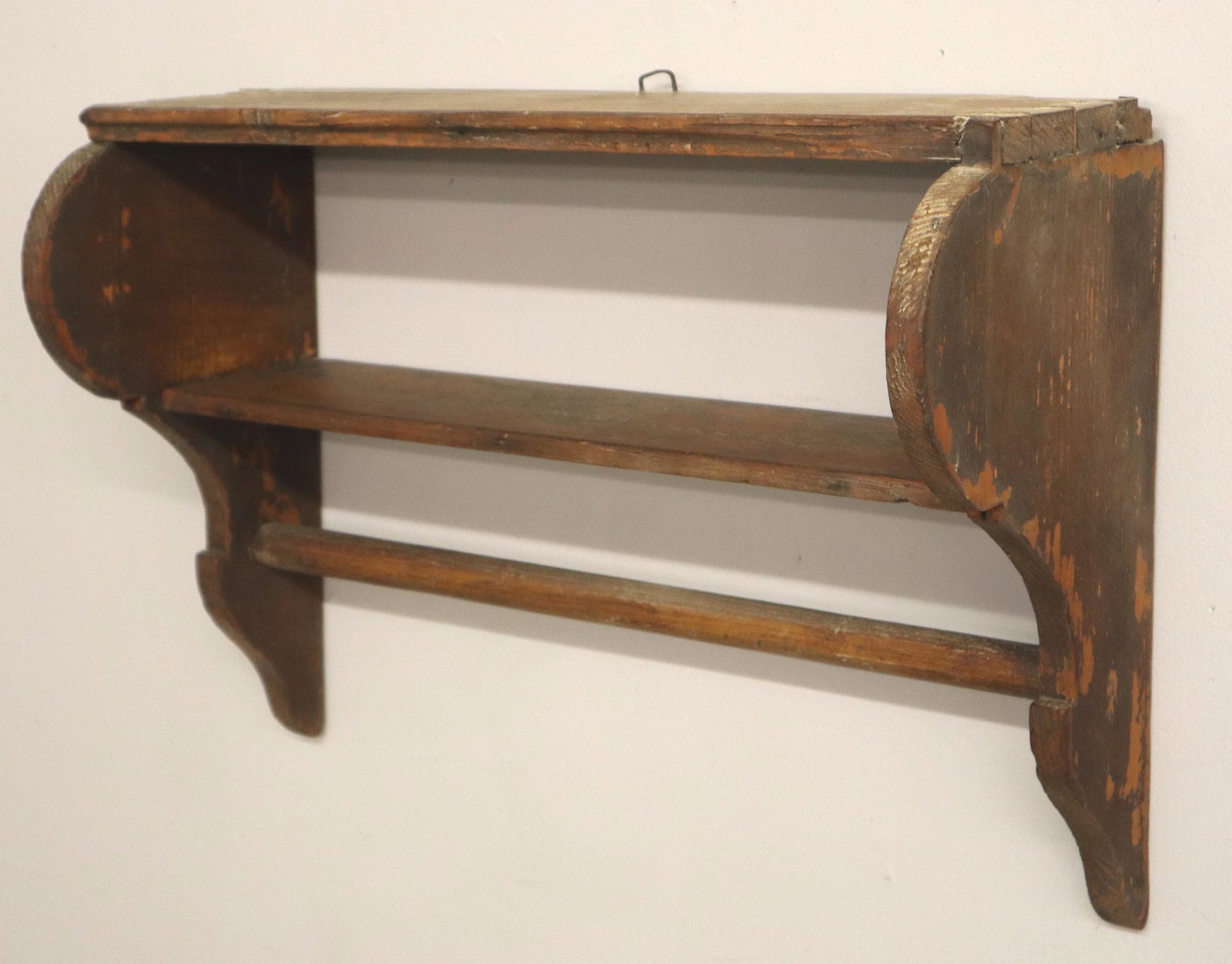 Primitive Wall Shelf: A late 19th century wall shelf. Dovetailed construction with shaped ends and lower towel bar. Old Red/Brown painted finish with wear and minor damage. 22 x 8 x 16" high. ESTIMATE $100-150