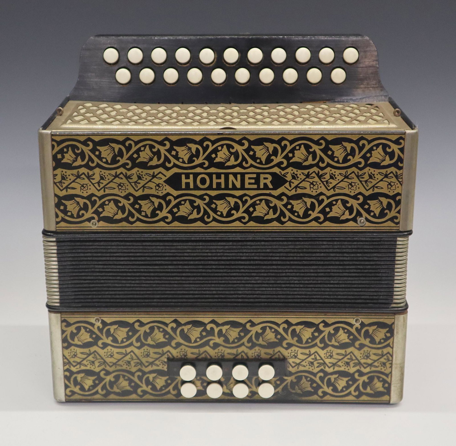 Hohner Accordion: An early 20th century Hohner accordion. 21 key, 2 row, 8 Bellow model with Gold "Pokerwork" painted decoration. Minor surface wear, leather pull strap and one closure strap are present but broken. 11"