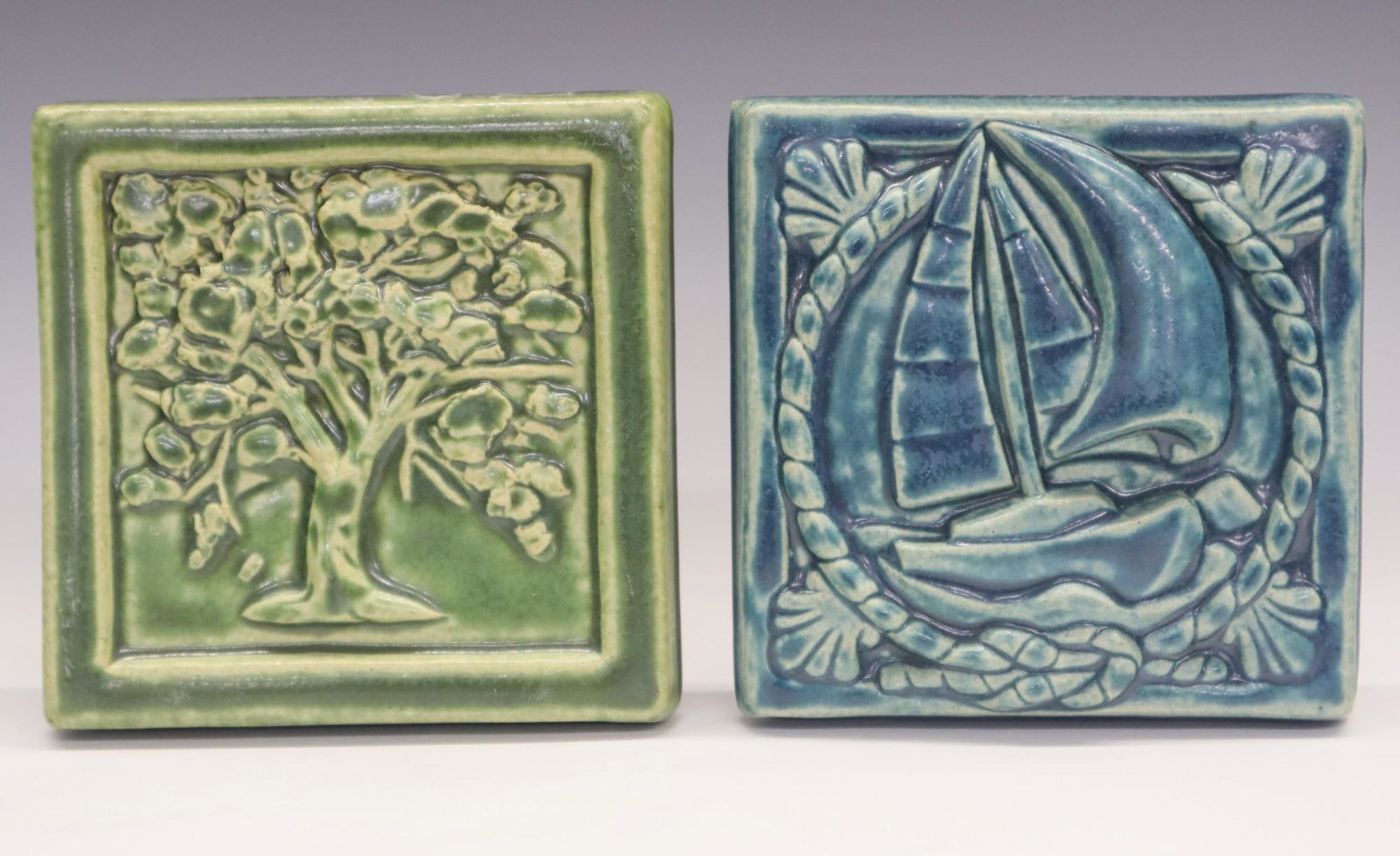 2 Pewabic Pottery Tiles: Two Pewabic Pottery tiles. Includes a 2016 tile with a sailboat and an undated tile with an Oak tree. Impressed marks. Slight wear. Approx 5 1/4" square. ESTIMATE $100-150