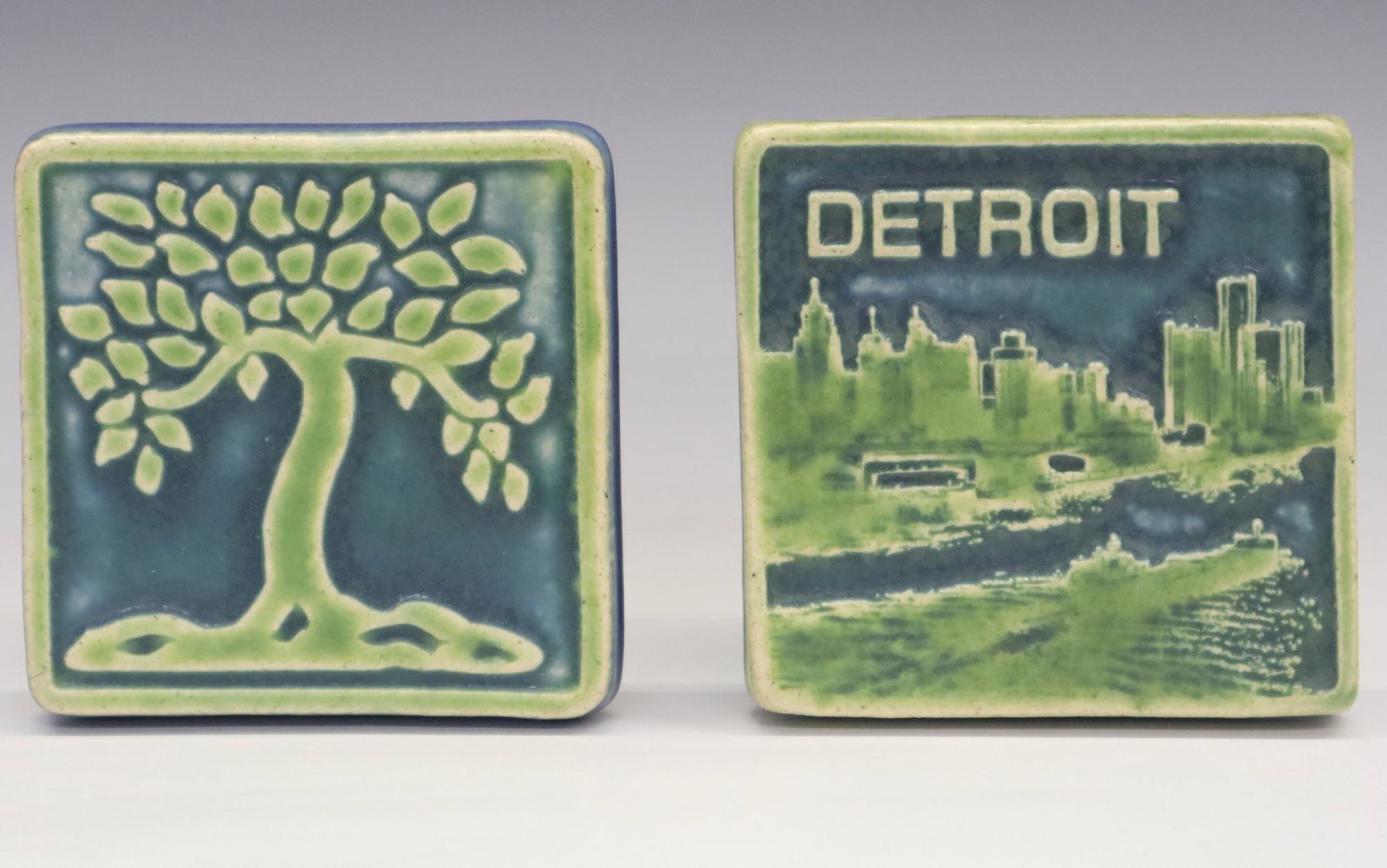 2 Pewabic Pottery Tiles: Two Pewabic Pottery tiles. Includes a 2014 tile with The Detroit River and a 2017 tile with a tree. Impressed marks. Slight wear. Approx 4" square. ESTIMATE $100-150