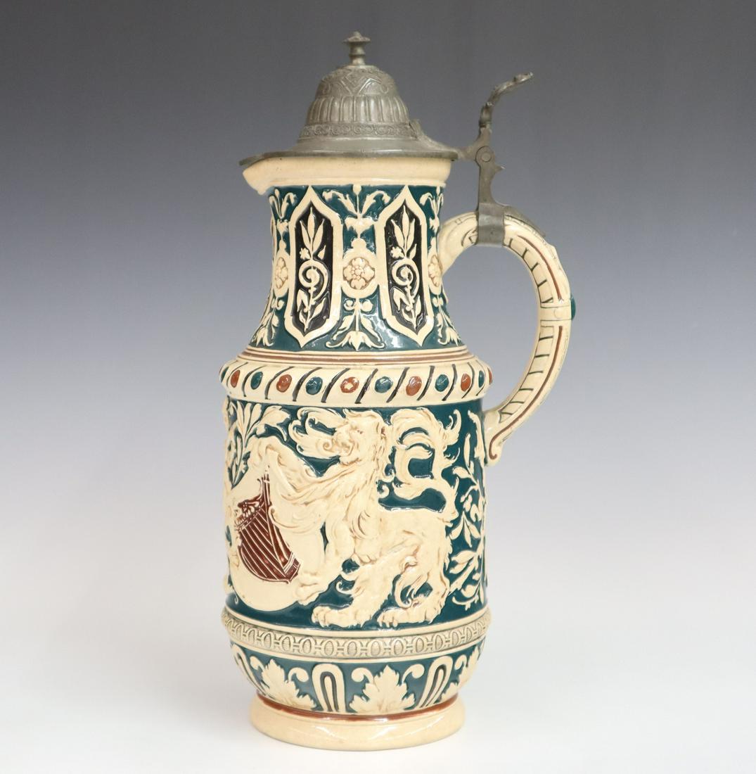 German Earthenware Stein: A turn of the century German earthenware stein, with mottos and coat of arms in relief. Impressed numeral mark. Minor wear. 14 1/2" high. ESTIMATE $100-200