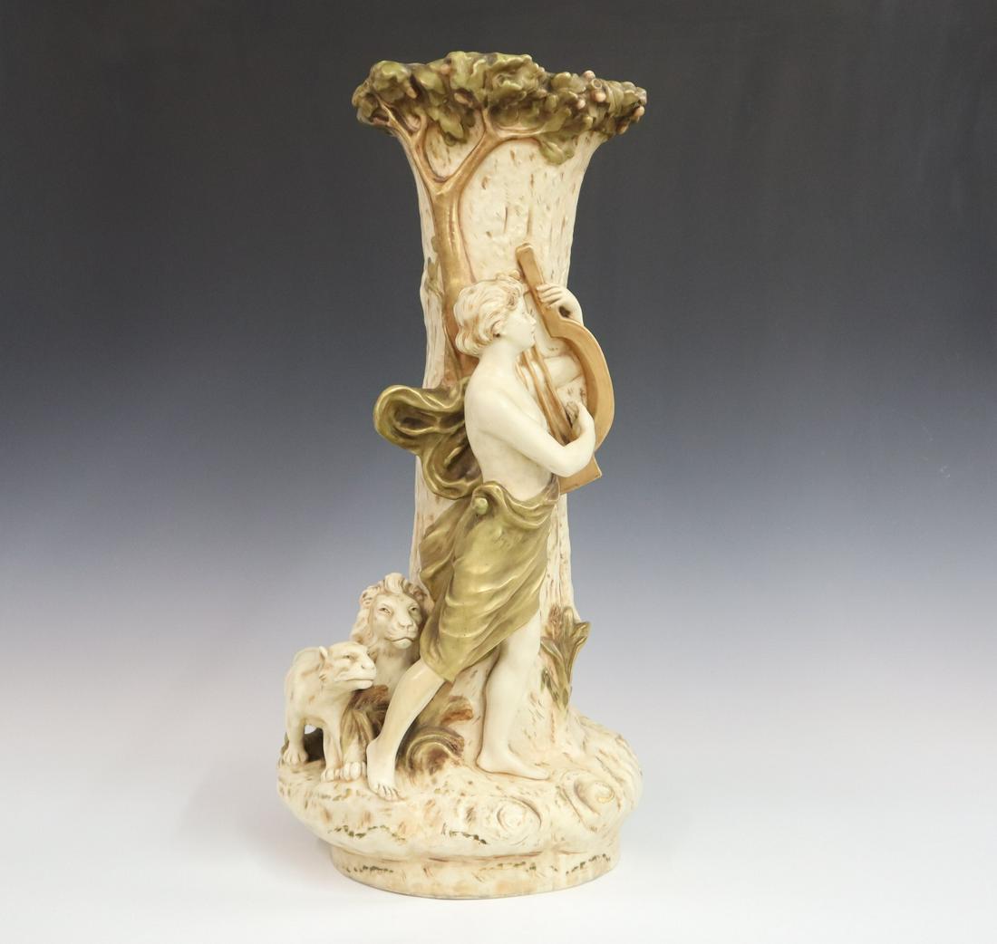 Royal Dux Vase: A large early 20th century Royal Dux vase, organic form with sculpted and applied figures; including a standing man playing a harp and two lions; in an ivory matte glaze with green and gold decoration