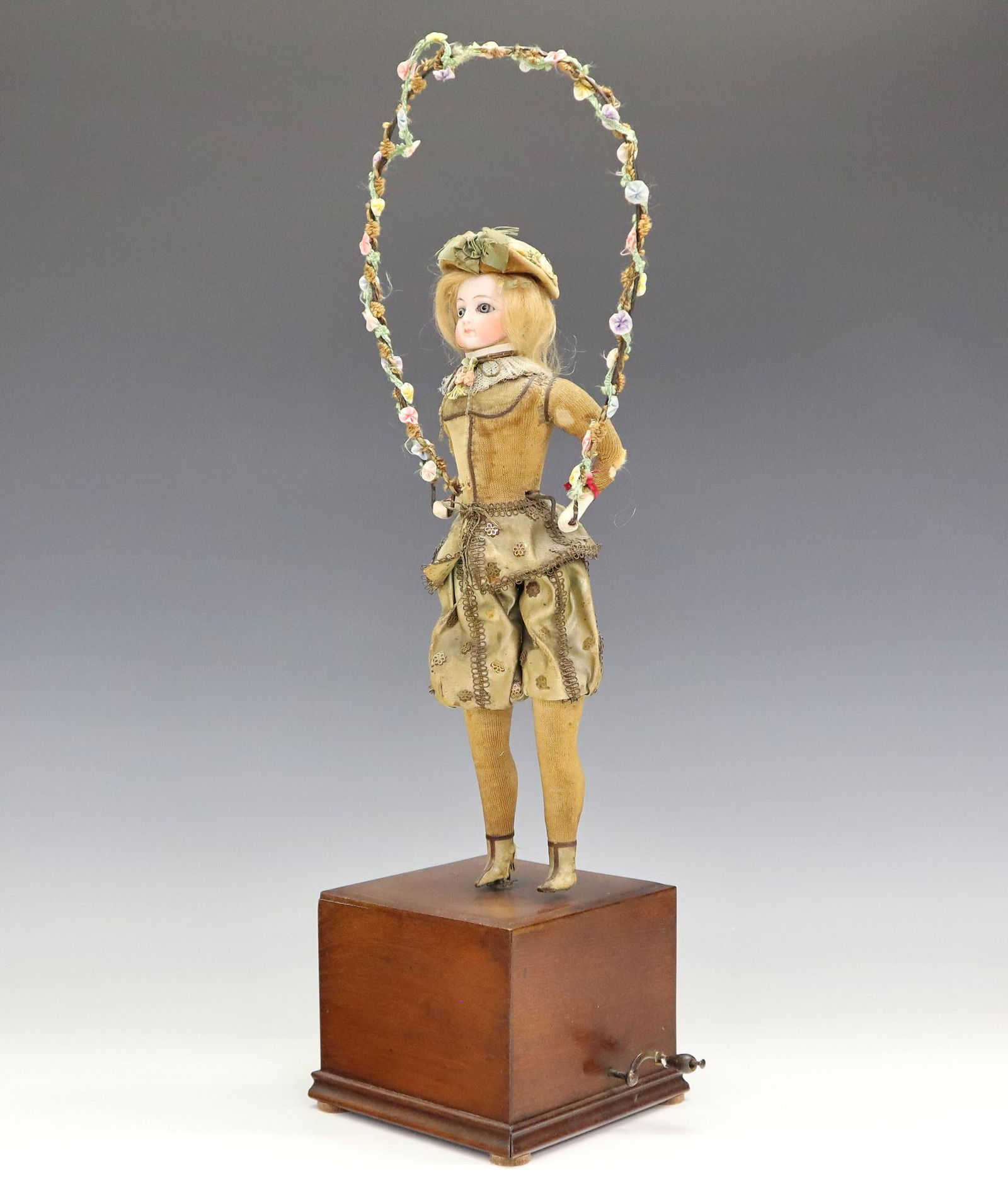 French Automaton: A late 19th century French Automaton of a young girl jumping rope. Papier mache figure with porcelain head and hands, fabric clothing and a wire jump rope on a Mahogany base with hand crank. Wear, som