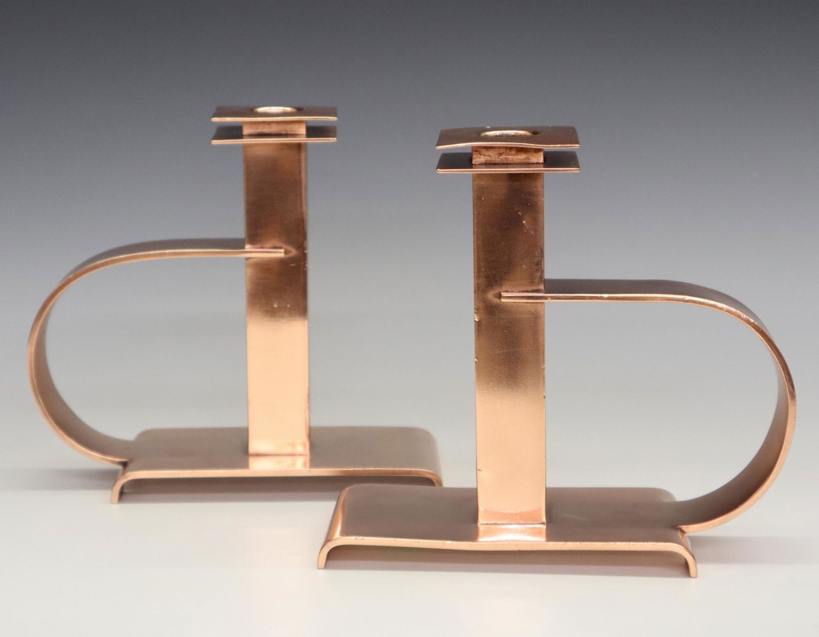 Pr. Albert Reimann Candlesticks: A Pair of Albert Reimann "Dee" Handle Copper Candlesticks. For Chase Brass & Copper Co., c. 1930. Impressed with maker's mark and "Design by Reimann" at the underside. Slight dings, nicks, and scratch