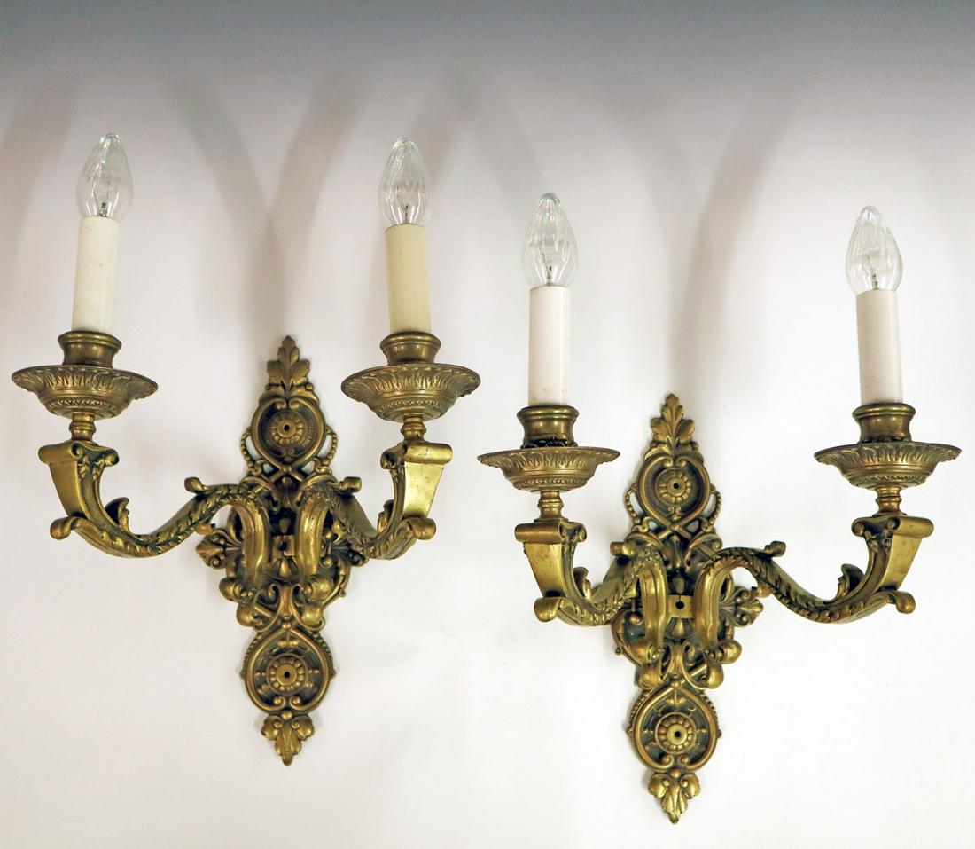 Pair of Cast Bronze Wall Sconces: Pair of 1920s cast bronze wall sconces. Each with two arms and classical decoration. Overall tarnish and older wiring. Repaired casting flaws to both, Left arm of one sconce shows a 3/8" split. ESTIMA