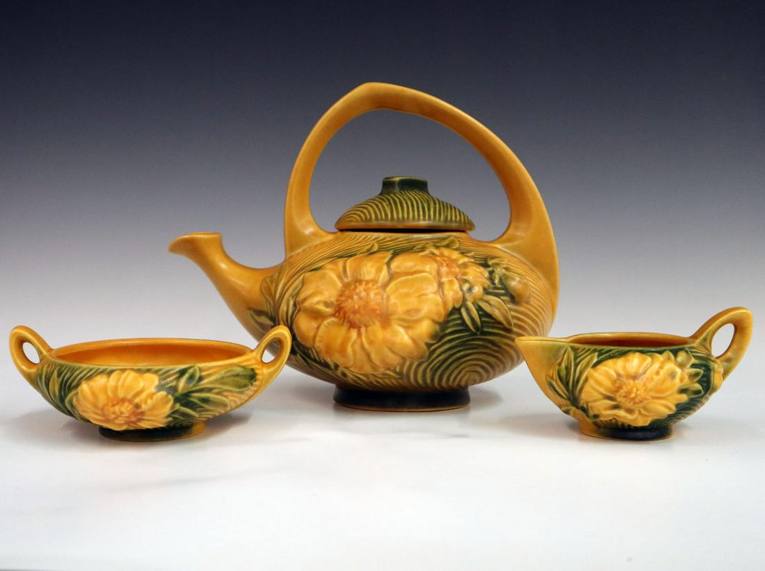 Roseville Tea Set: A 1940s Roseville Pottery "Peony" Pattern Tea set. Three piece set in yellow, consists of tea pot, creamer and sugar bowl. All three marked "Roseville, USA." 1/32" diameter flake to rim of tea pot. Up