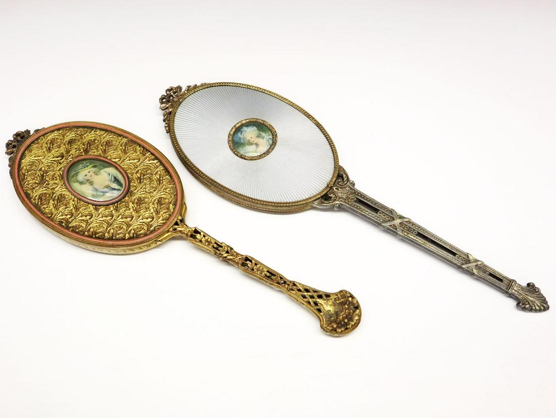 2 Apollo Hand Mirrors: Two 1920s-1930s Apollo Studios Hand Mirrors. Including 1 gilt metal hand mirror and 1 two-toned metal hand mirror; each with beveled glass mirror and mounted with hand decorated portrait reserve. Both