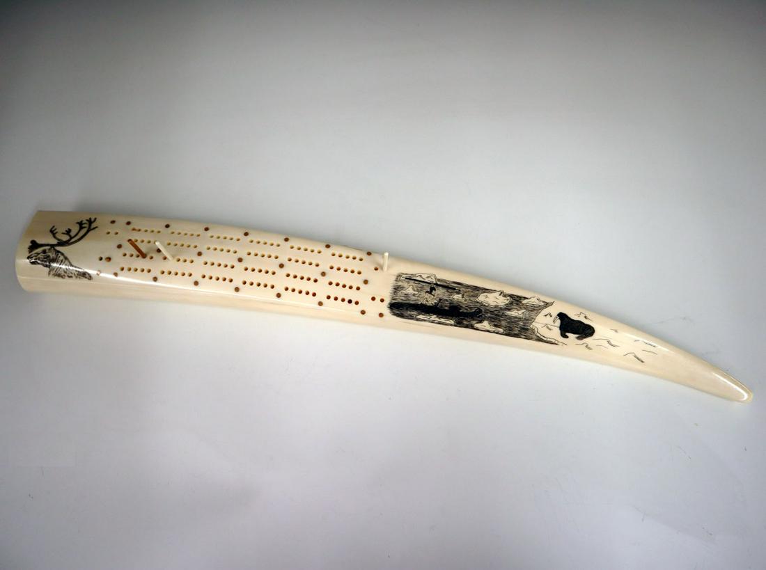 Scrimshaw Cribbage Board.: A 1960s Alaskan Scrimshaw Cribbage Board. Decorated with motifs of a walrus, a hunter in a kayak, and a Caribou; by artist Francis Kakoona, Shushana, Alaska. Minor wear and some age cracks. 21" long. 