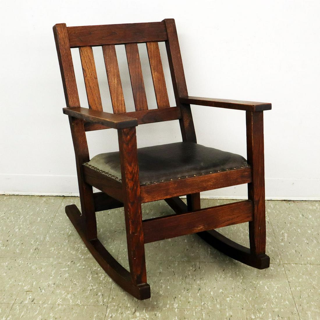 Arts & Crafts Rocking Arm Chair: A Turn of the Century Arts & Crafts Rocking Arm Chair. Oak construction with 4-slat back and through tenon arms; distressed black leather seat and original finish. Nicks and scratches on a dry finish,
