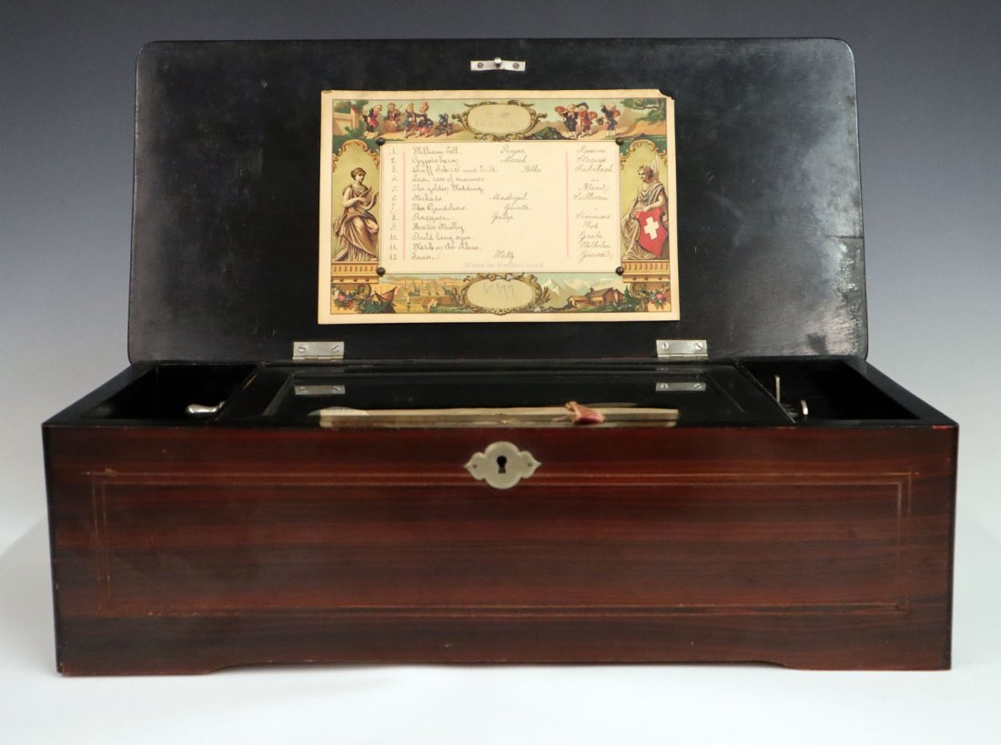 Swiss Music Box: A Turn of the Century Swiss Music Box. Having 12 tunes and within a grained Rosewood painted case with lithographed tune card at the interior of the cover. Runs sluggish. Minor wear to paint. 16 3/4 x
