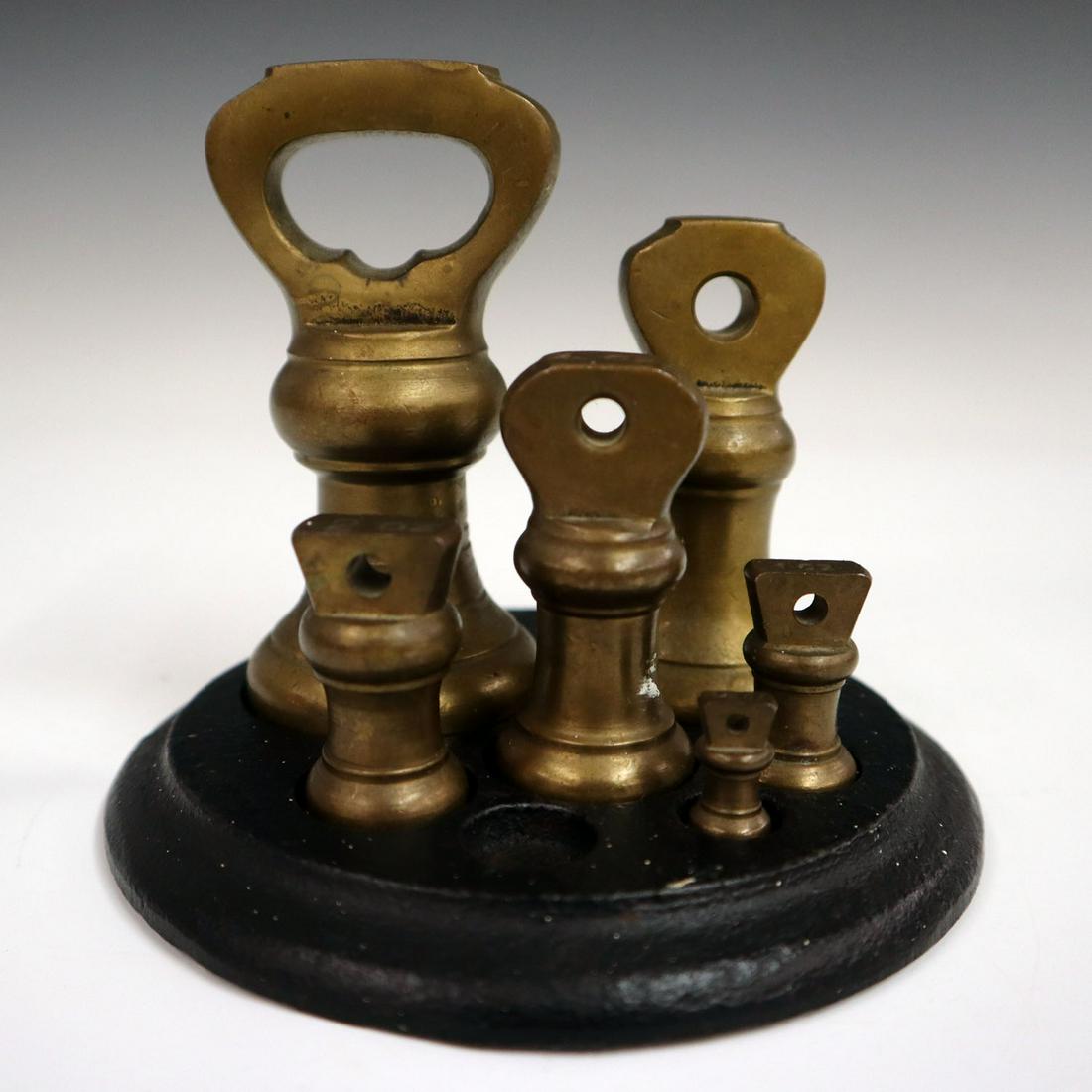 Brass Bell Weights: An Incomplete Set of 19th Century British Brass Bell Weights. In a period cast iron holder with molded base. The 1/2 oz is missing. Tarnish evident. Up to 3 3/4" high. ESITMATE $50-100