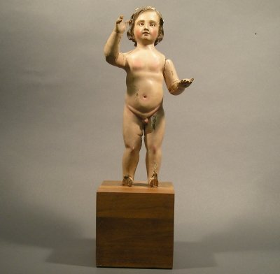 Santos: An early 20th century Spanish Colonial carved wooden Santos of the Christ Child. Original painted surface. Wear, flaking, older restoration and loss at feet. On a Walnut stand, 12 1/2" high.