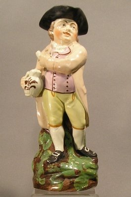 Toby Jug: A mid 19th century English Staffordshire Toby jug. Multi-color glaze decoration with enameled detail. Standing version with jug and pipe. Minor wear, some flaking to the enameling. 11" high.