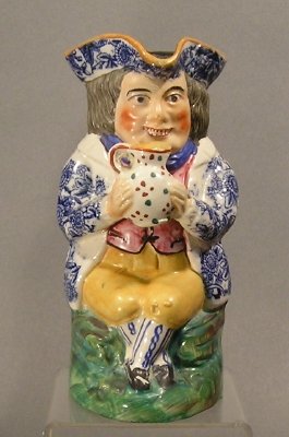 Toby Jug: A mid 19th century English Staffordshire Toby jug. Multi-color glaze decoration with Blue transfer jacket. Standing version with outstretched arms. Minor wear, some flaking to the enameling. 7 1/4" hi