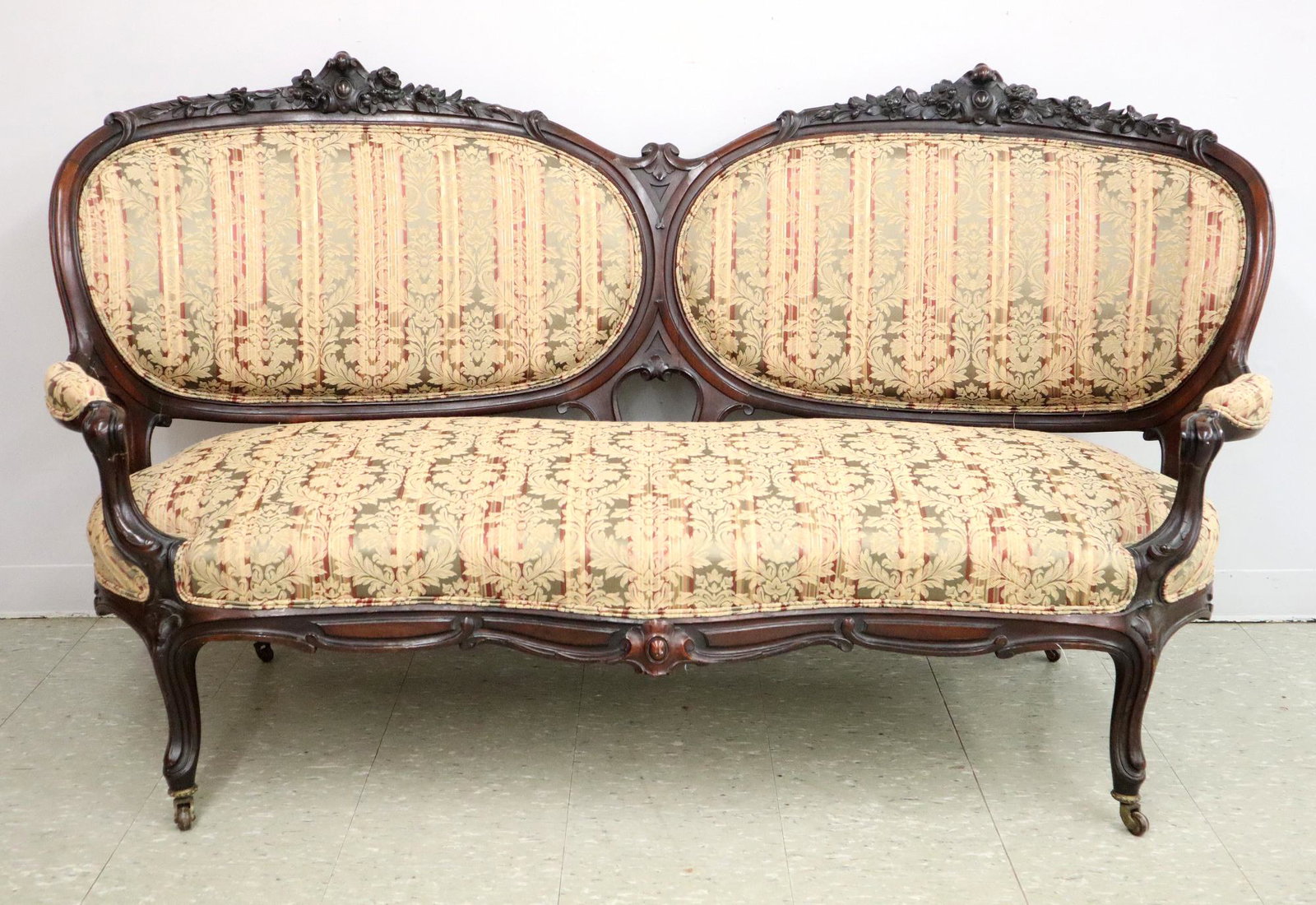 American Victorian Sofa: A Mid-19th century American Victorian Period Walnut Sofa. Double medallion back with floral carved crest, open arms, and shaped skirt. Old repair on rail near back leg, reupholstered with slight wear,