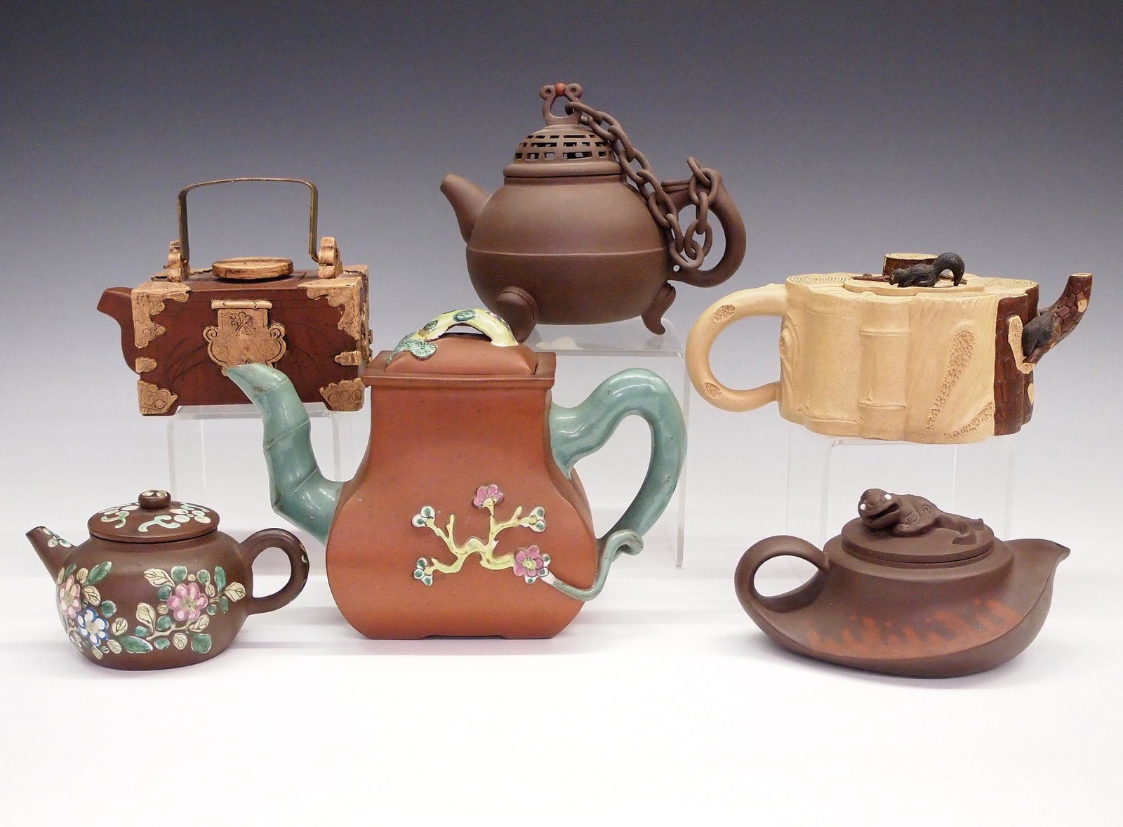 6 Chinese Earthenware Teapots: A collection of six 20th century Chinese earthenware teapots. Various designs include two with creature covers, two with enameled detail, one with linked cover and another with brass handle. Impressed