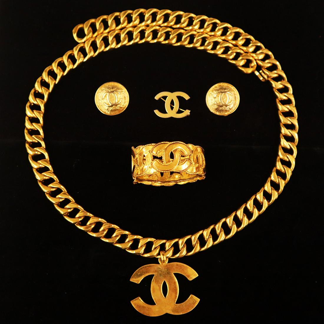 Chanel Collectors Group: A Chanel collectors group. Chain-link style gold tone belt with logo pendant suspended from the middle, with oval plaque maker's mark, together with a pair of ear clips, a brooch, and a cuff style bra