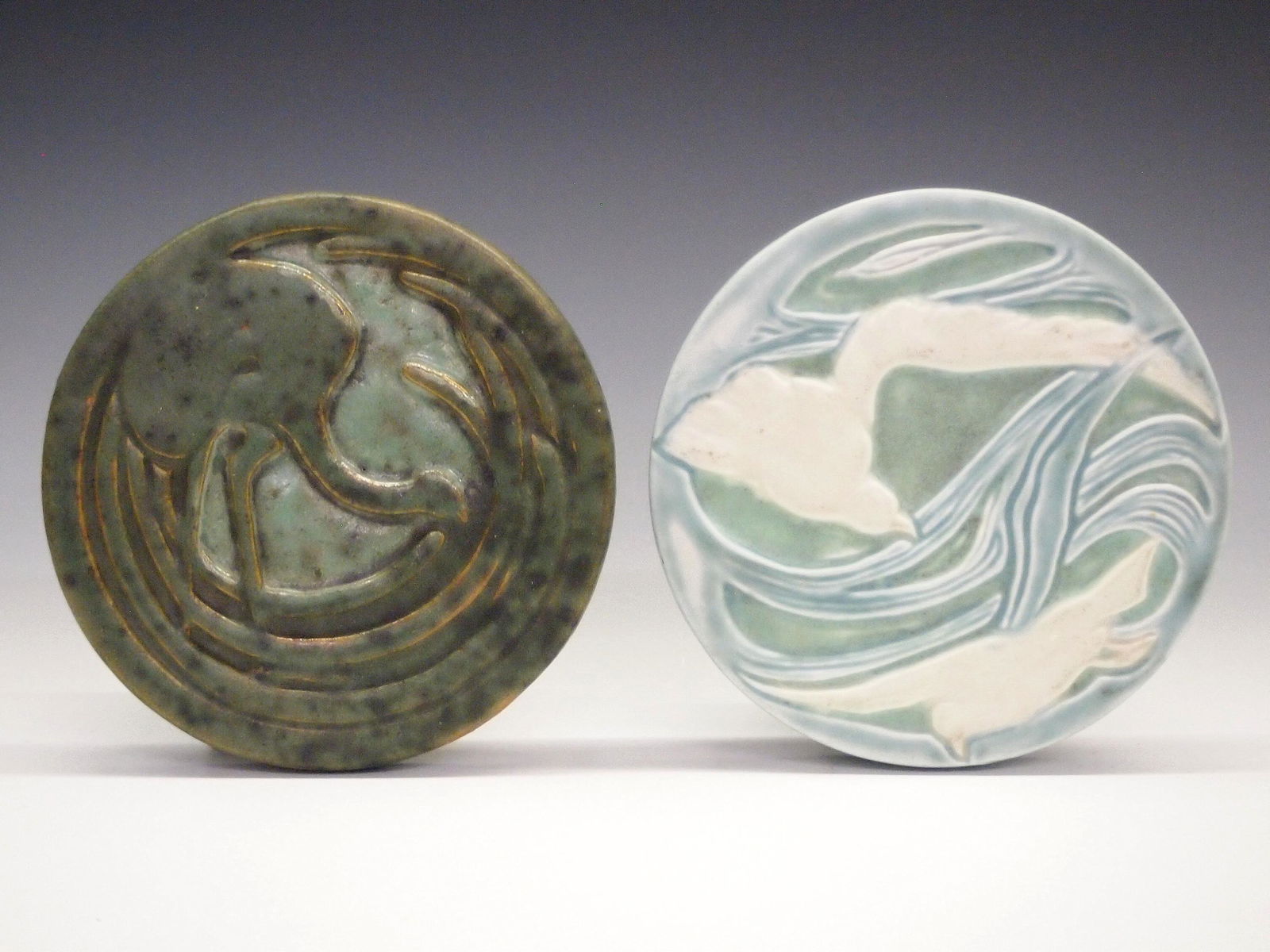 2 American Ceramic Trivets: Two American ceramic trivets. Including one unmarked Fulper trivet depicting a stylized exotic bird in a Green matte glaze with "David Rago Gallery American Art tile 1880-1950" label verso and a Rookw