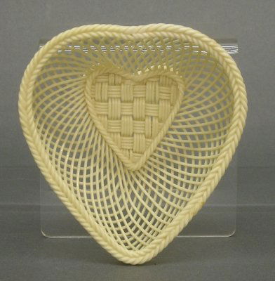 Belleek Basket: An Irish Belleek woven porcelain Heart shaped basket. Ivory glaze. Two applied banners read "Belleek" and "Ireland". Slight wear. 4 3/4" long. ESTIMATE $50-100