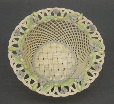 Belleek basket: An Irish Belleek woven porcelain basket. "Forget me not" pattern in an Ivory glaze with multicolor floral decoration. Applied cushion with brown printed mark. Slight wear. 6" diameter. ESTIMATE $100-2