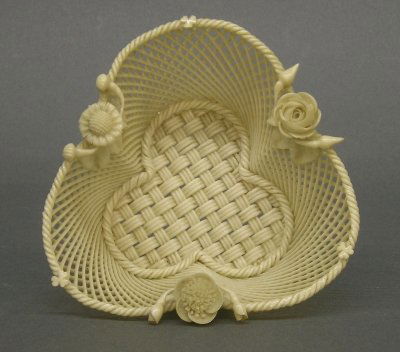Belleek basket: An Irish Belleek woven porcelain Shamrock shaped basket. Ivory glaze with applied floral decoration. Two applied banners read "Belleek" and "Co Fermanagh". Slight wear. 5" long. ESTIMATE $200-300