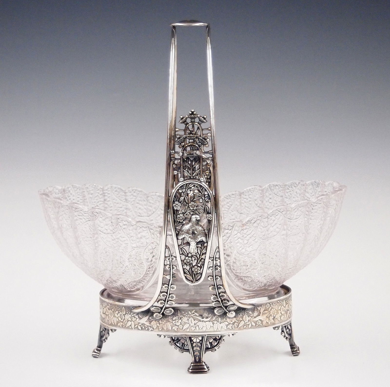 Meriden Brides Basket: A turn of the century Meriden brides basket. Molded glass bowl with quadruple plate frame with song birds in a garden. Some surface wear, lacks serving fork. 11" high. ESTIMATE $100-150